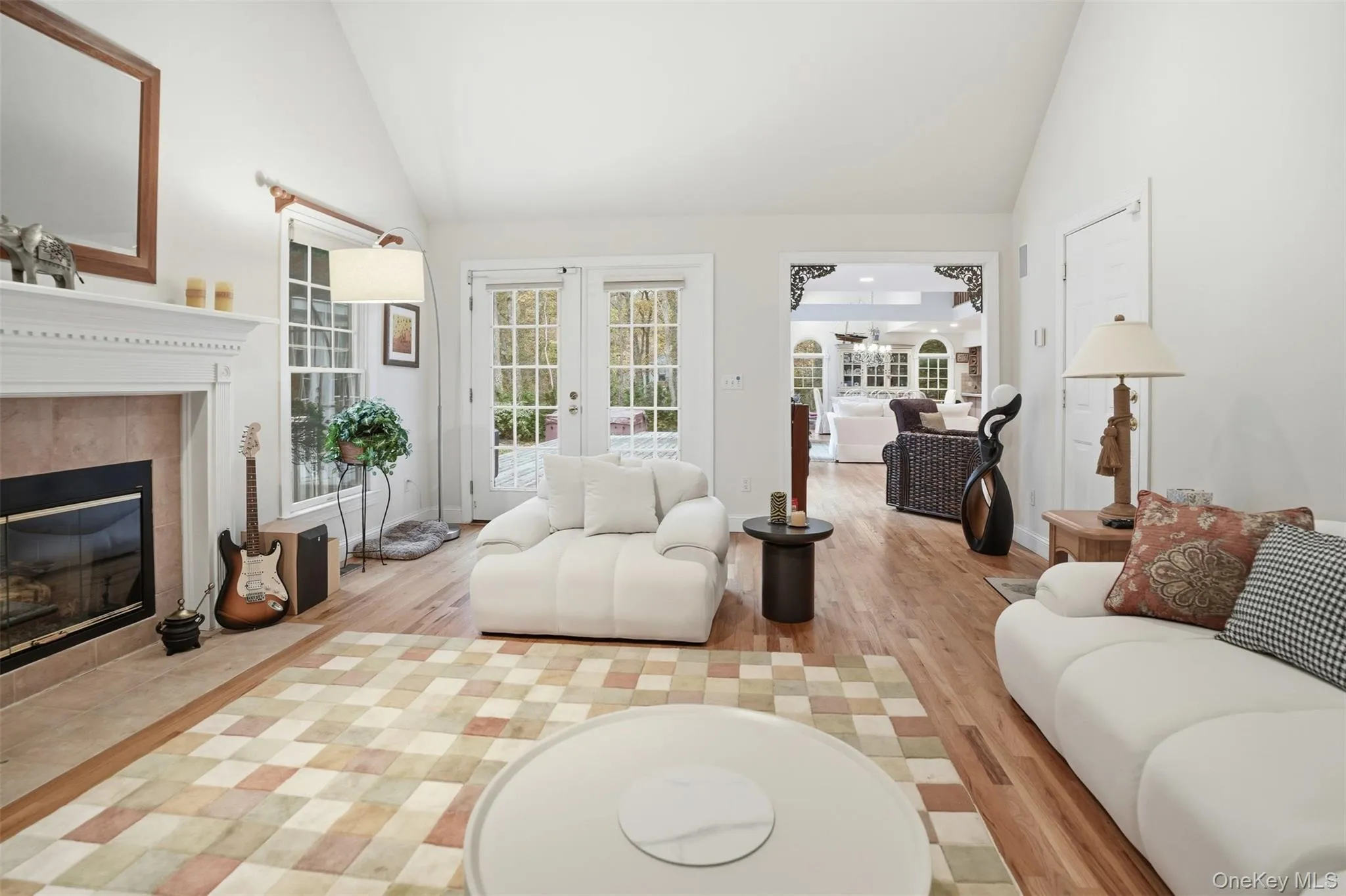 Living area with a tiled fireplace, high vaulted ceiling, light wood-style floors, and french doors Living area with a tiled fireplace, high vaulted ceiling, light wood-style floors, and french doors