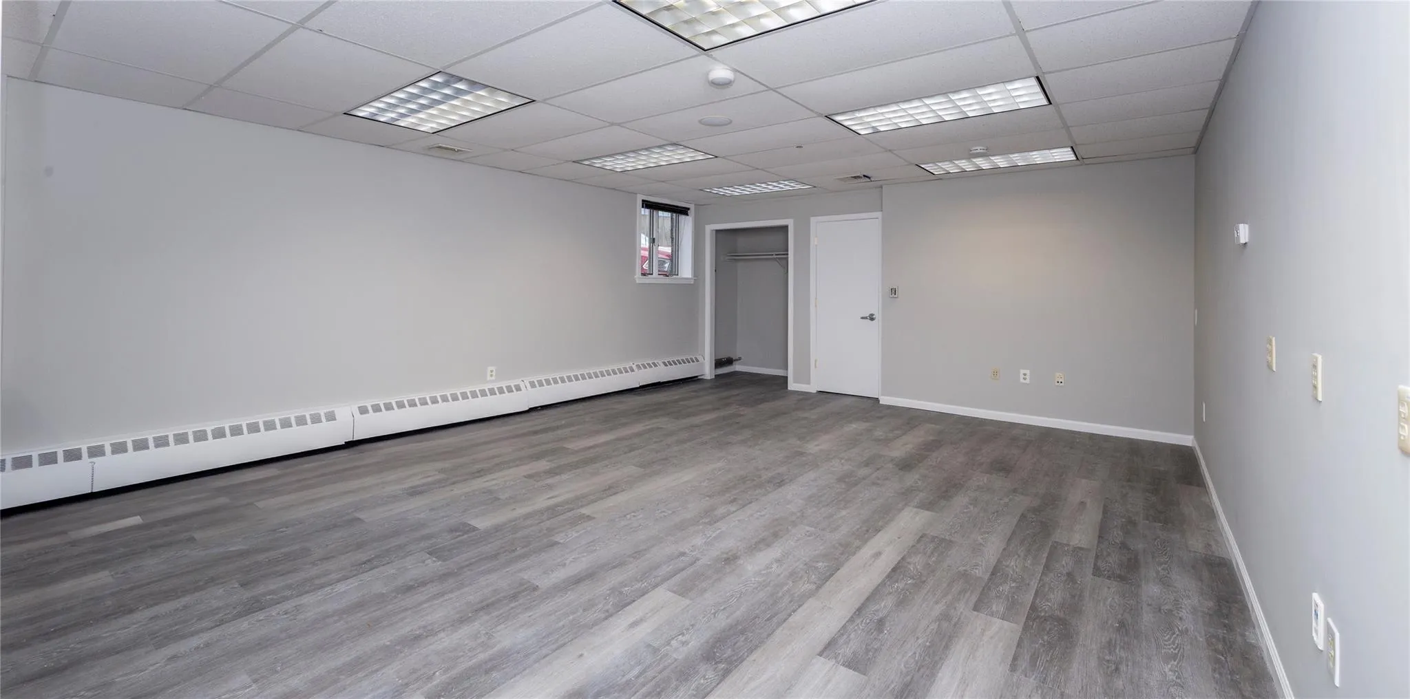 Empty room with a drop ceiling, a baseboard radiator, baseboards, and wood finished floors Empty room with a drop ceiling, a baseboard radiator, baseboards, and wood finished floors