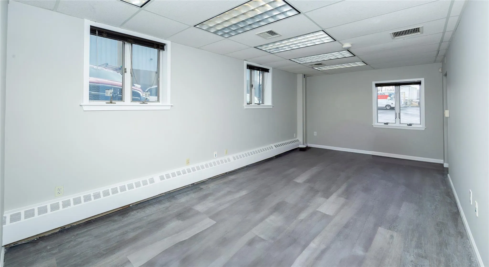 Unfurnished room featuring wood finished floors, visible vents, a drop ceiling, and a baseboard radiator Unfurnished room featuring wood finished floors, visible vents, a drop ceiling, and a baseboard radiator