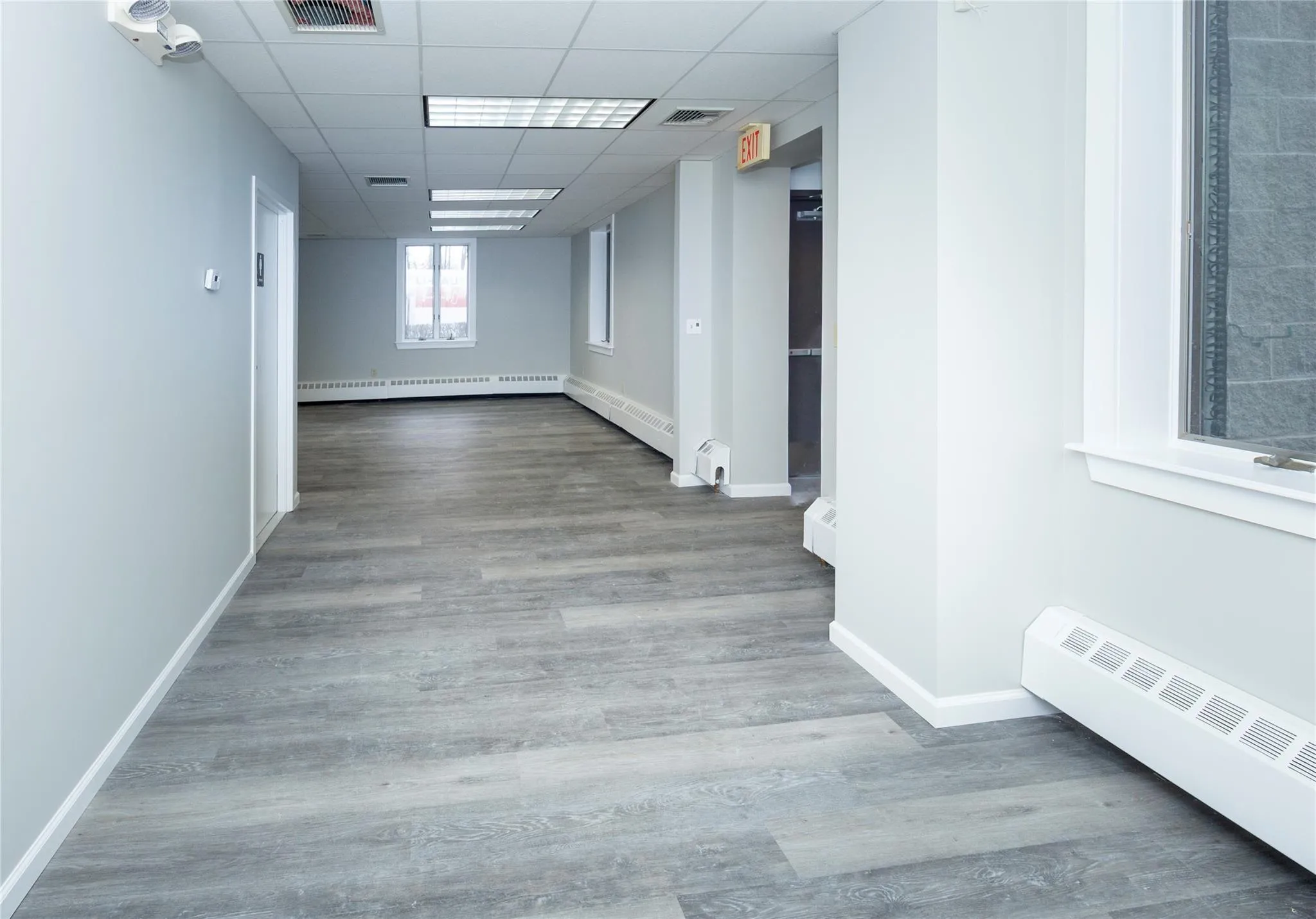 Hallway featuring a drop ceiling, a baseboard heating unit, wood finished floors, radiator, and baseboards Hallway featuring a drop ceiling, a baseboard heating unit, wood finished floors, radiator, and baseboards