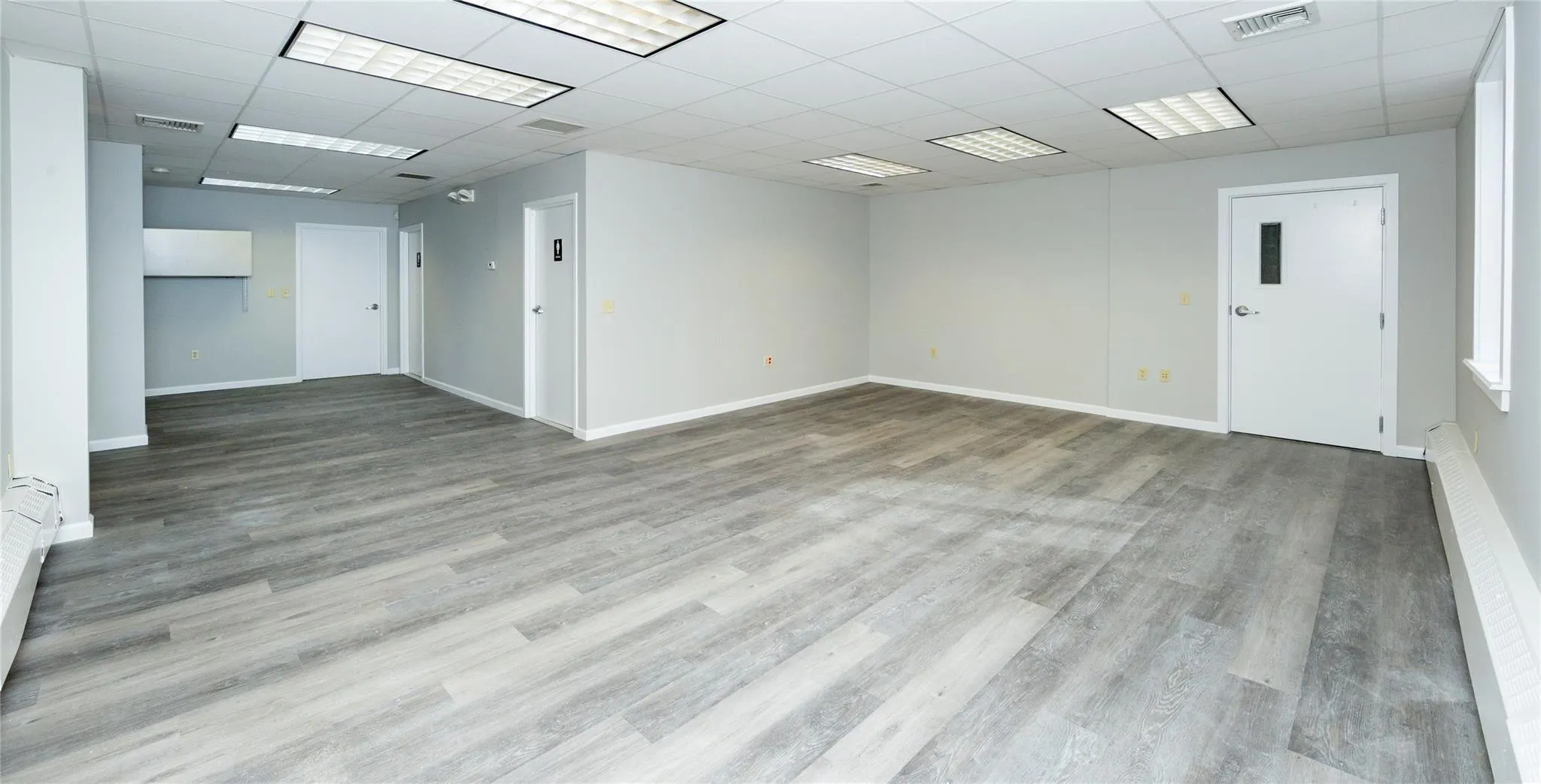 Empty room with baseboards, wood finished floors, visible vents, and a paneled ceiling Empty room with baseboards, wood finished floors, visible vents, and a paneled ceiling