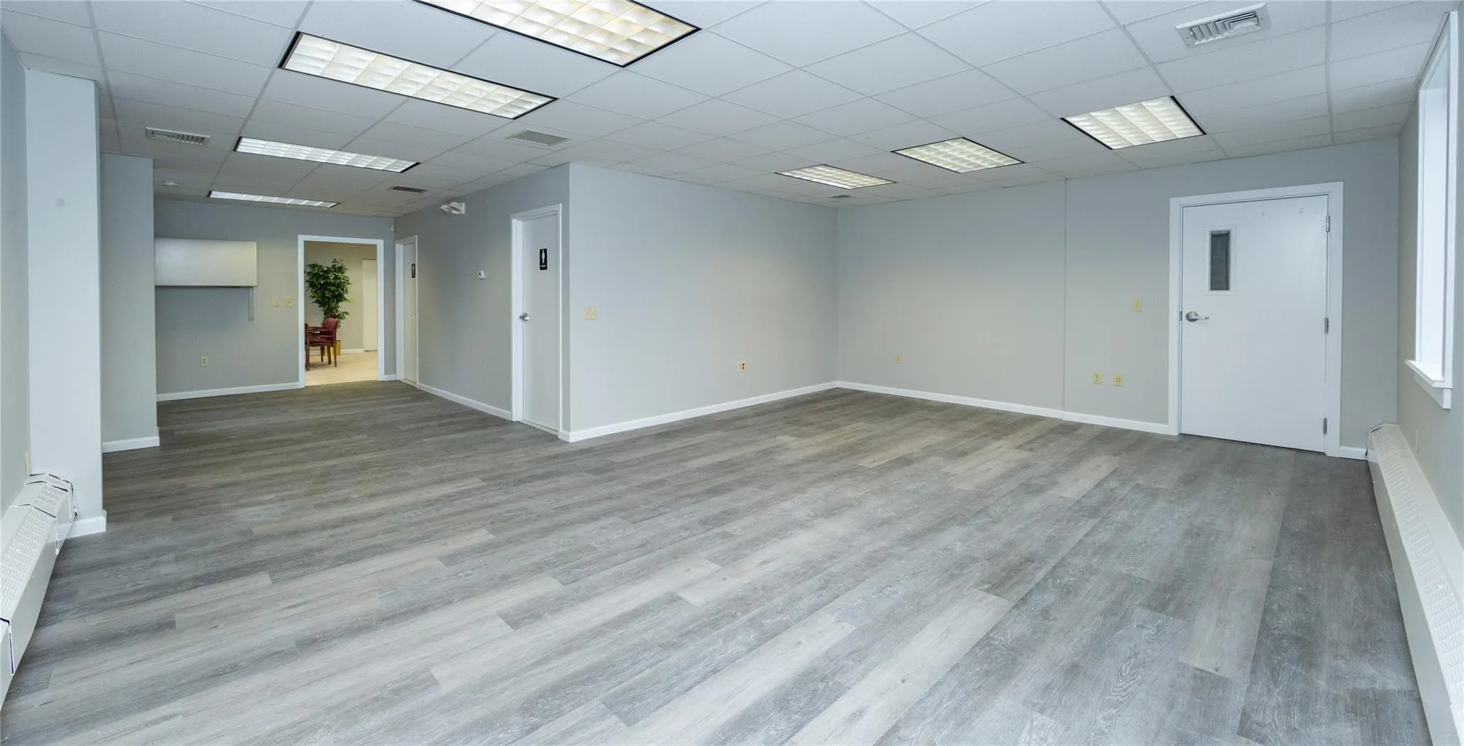 Empty room featuring visible vents, a baseboard heating unit, baseboards, a drop ceiling, and wood finished floors Empty room featuring visible vents, a baseboard heating unit, baseboards, a drop ceiling, and wood finished floors