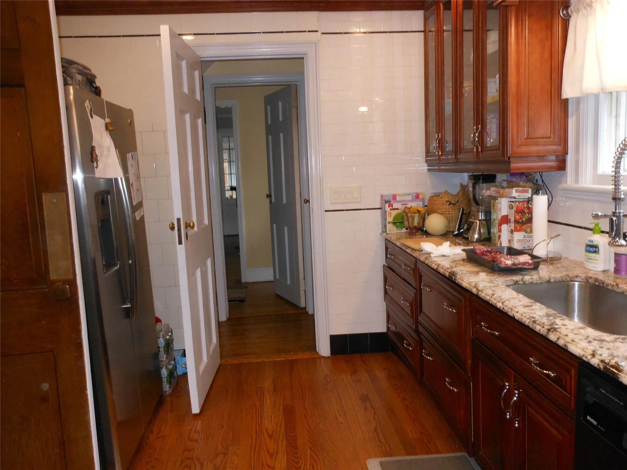 Kitchen with a sink, dark wood-type flooring, glass insert cabinets, dishwasher, and stainless steel fridge Kitchen with a sink, dark wood-type flooring, glass insert cabinets, dishwasher, and stainless steel fridge