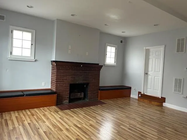 Unfurnished Open Space featuring wood floors and a brick fireplace Unfurnished Open Space featuring wood floors and a brick fireplace