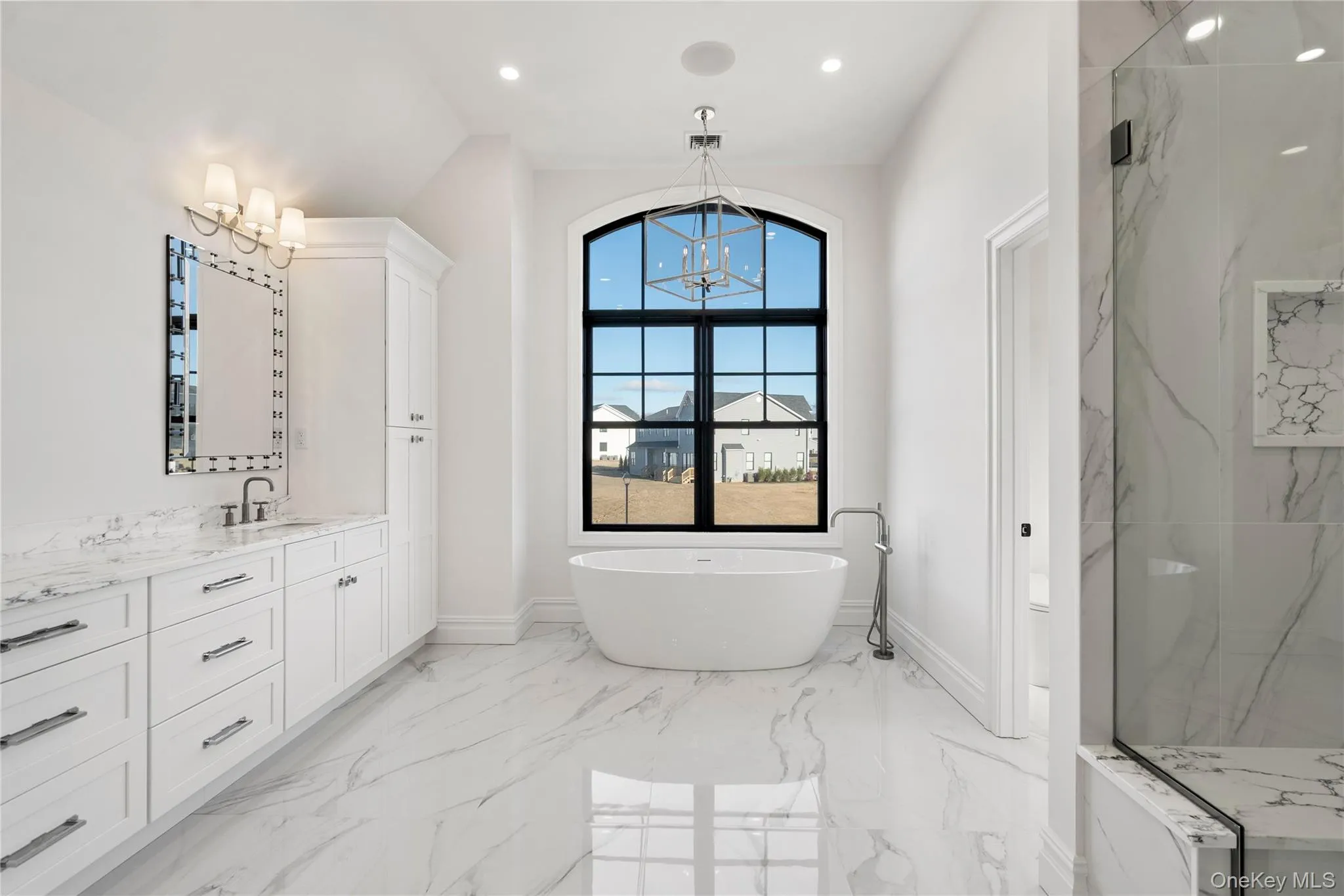 Full bath featuring a chandelier, vanity, a freestanding tub, light marble finish floors, and a marble finish shower Full bath featuring a chandelier, vanity, a freestanding tub, light marble finish floors, and a marble finish shower