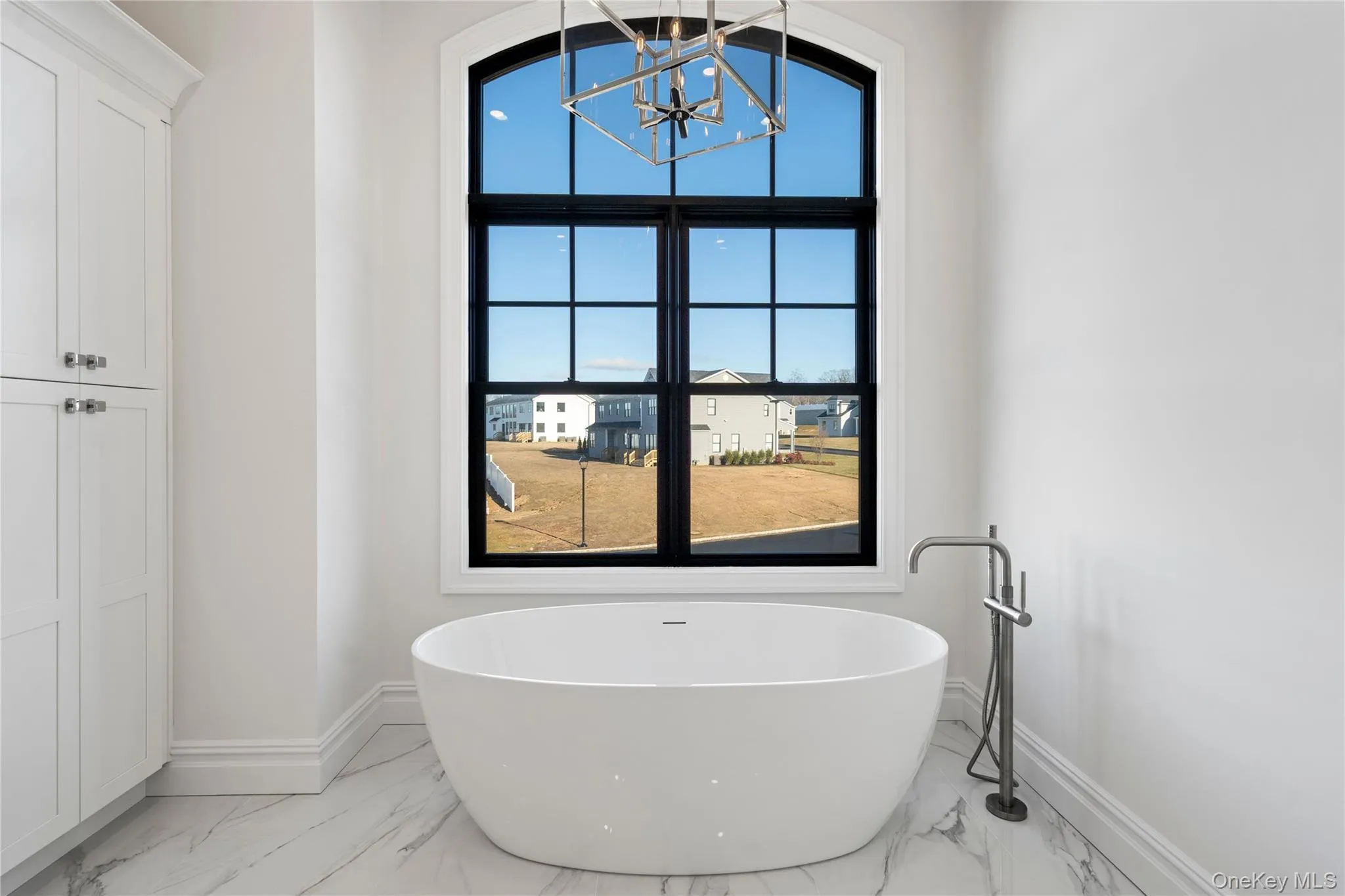Full bathroom with light marble finish floors, a chandelier, and a freestanding tub Full bathroom with light marble finish floors, a chandelier, and a freestanding tub