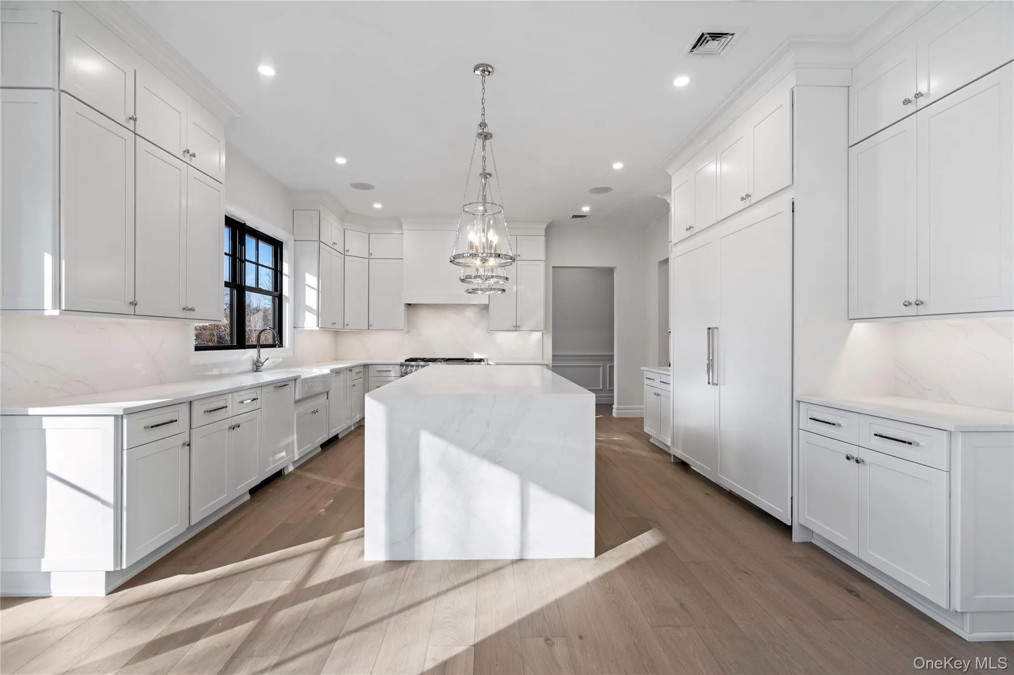 Kitchen with light stone countertops, pendant lighting, backsplash, white cabinetry, and a center island Kitchen with light stone countertops, pendant lighting, backsplash, white cabinetry, and a center island