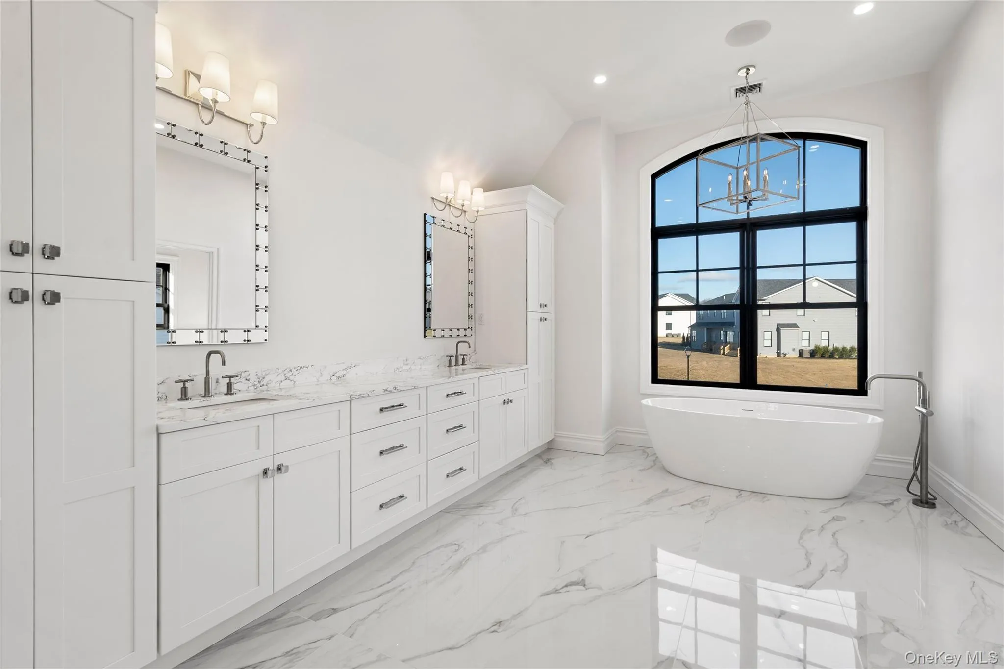 Full bath with double vanity, light marble finish flooring, a soaking tub, a chandelier, and vaulted ceiling Full bath with double vanity, light marble finish flooring, a soaking tub, a chandelier, and vaulted ceiling