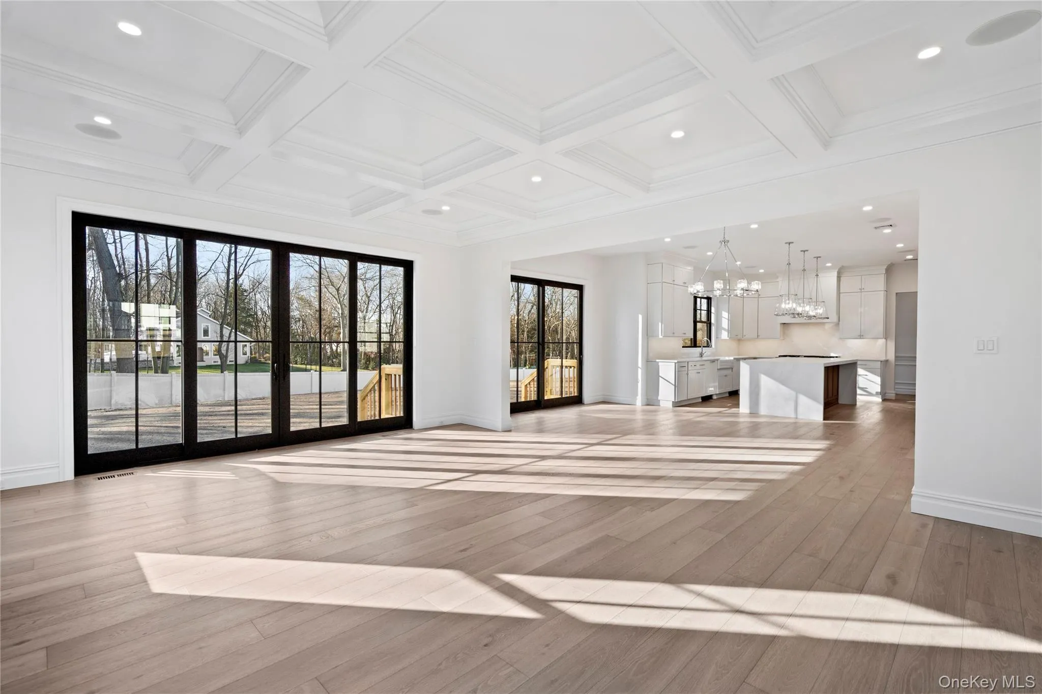 Unfurnished living room featuring light wood-type flooring, beam ceiling, coffered ceiling, recessed lighting, and a chandelier Unfurnished living room featuring light wood-type flooring, beam ceiling, coffered ceiling, recessed lighting, and a chandelier