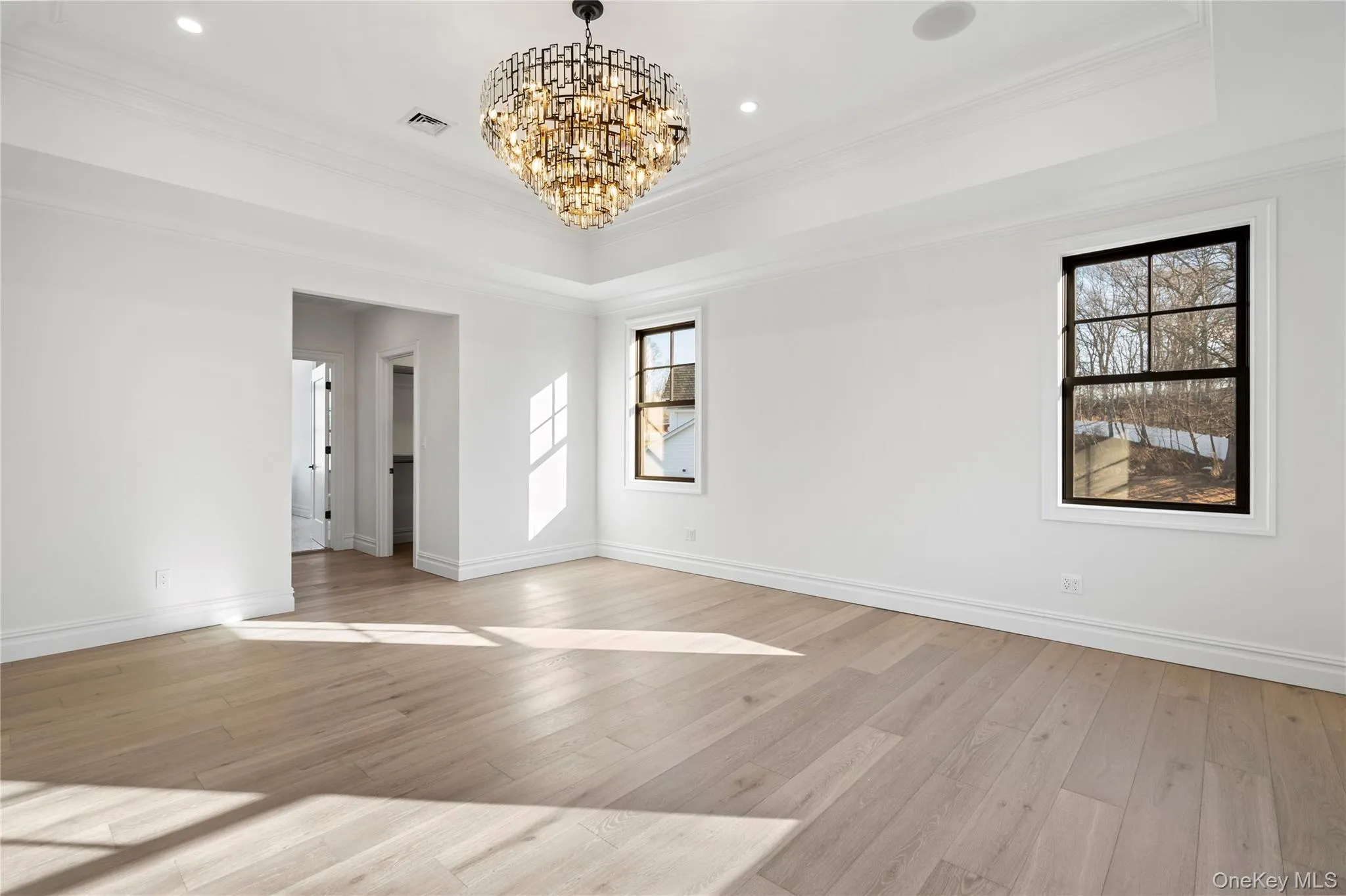Spare room featuring a tray ceiling, a chandelier, light wood-style floors, crown molding, and recessed lighting Spare room featuring a tray ceiling, a chandelier, light wood-style floors, crown molding, and recessed lighting