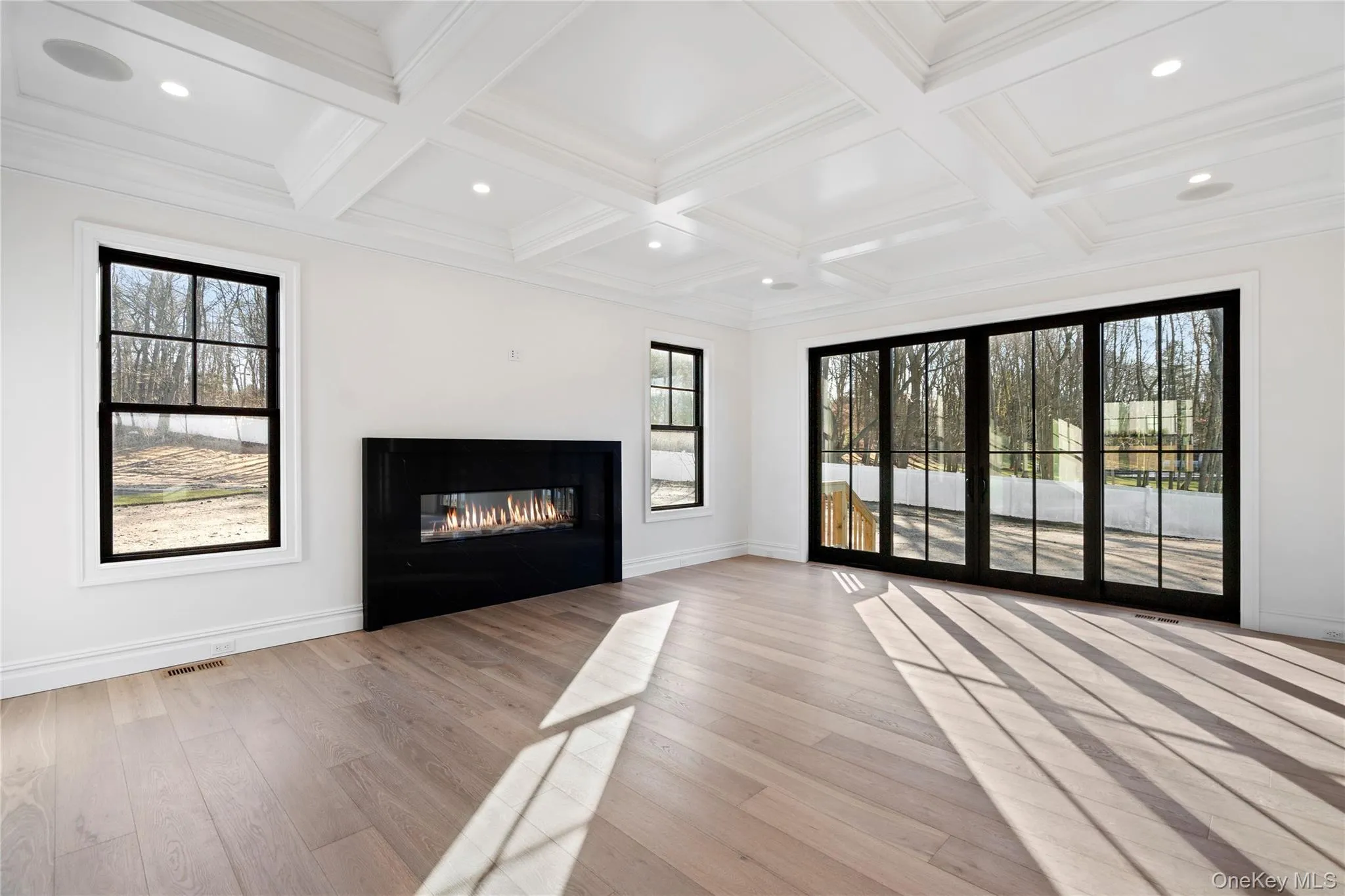 Unfurnished living room featuring light wood-type flooring, a glass covered fireplace, recessed lighting, coffered ceiling, and beam ceiling Unfurnished living room featuring light wood-type flooring, a glass covered fireplace, recessed lighting, coffered ceiling, and beam ceiling