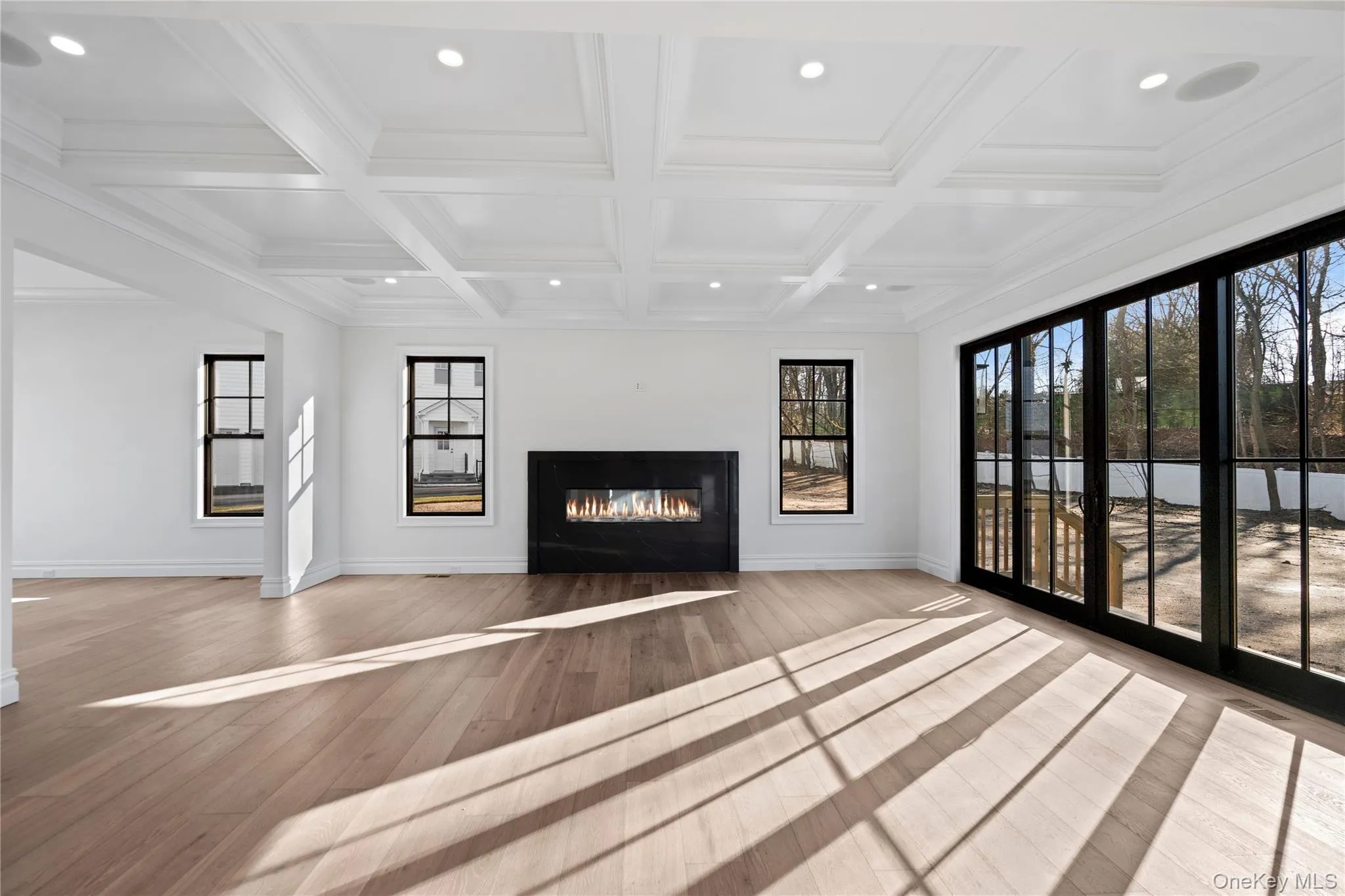 Unfurnished living room featuring recessed lighting, a glass covered fireplace, ornamental molding, beam ceiling, and wood finished floors Unfurnished living room featuring recessed lighting, a glass covered fireplace, ornamental molding, beam ceiling, and wood finished floors