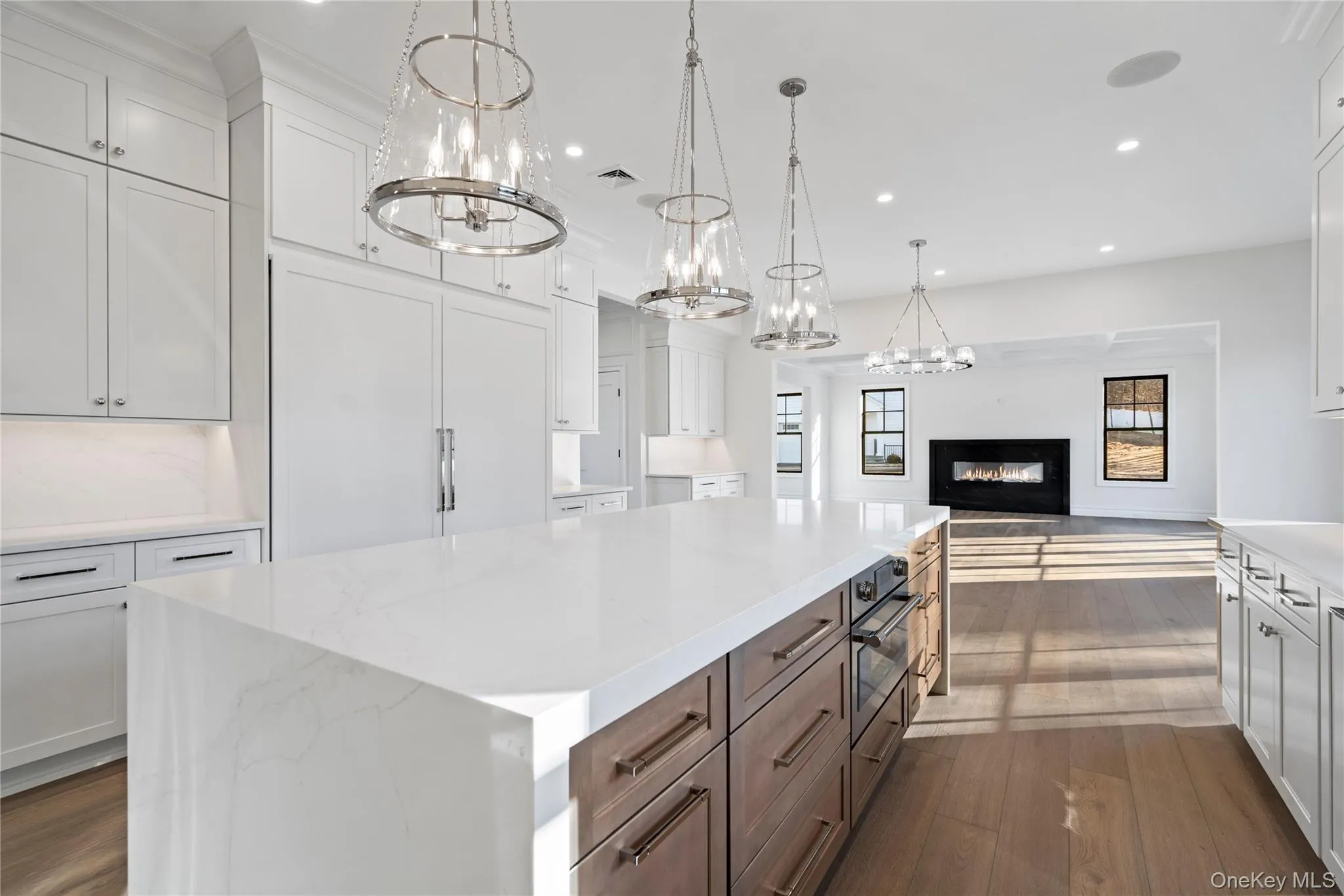 Kitchen featuring white cabinetry, light stone counters, a glass covered fireplace, a kitchen island, and a chandelier Kitchen featuring white cabinetry, light stone counters, a glass covered fireplace, a kitchen island, and a chandelier