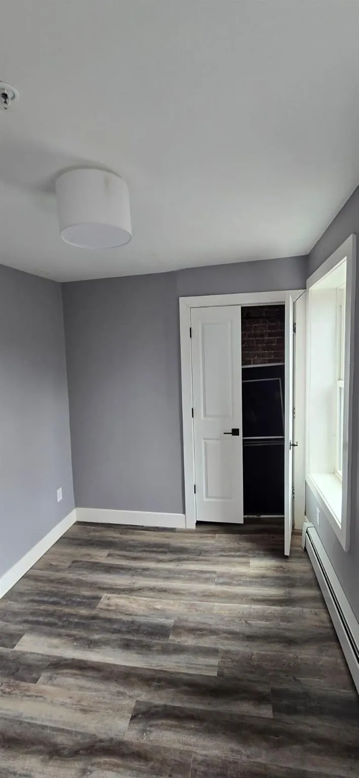 Unfurnished room with dark wood finished floors, baseboards, and baseboard heating Unfurnished room with dark wood finished floors, baseboards, and baseboard heating