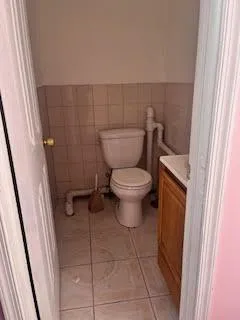 Half bath featuring vanity, wainscoting, tile patterned floors, toilet, and tile walls Half bath featuring vanity, wainscoting, tile patterned floors, toilet, and tile walls