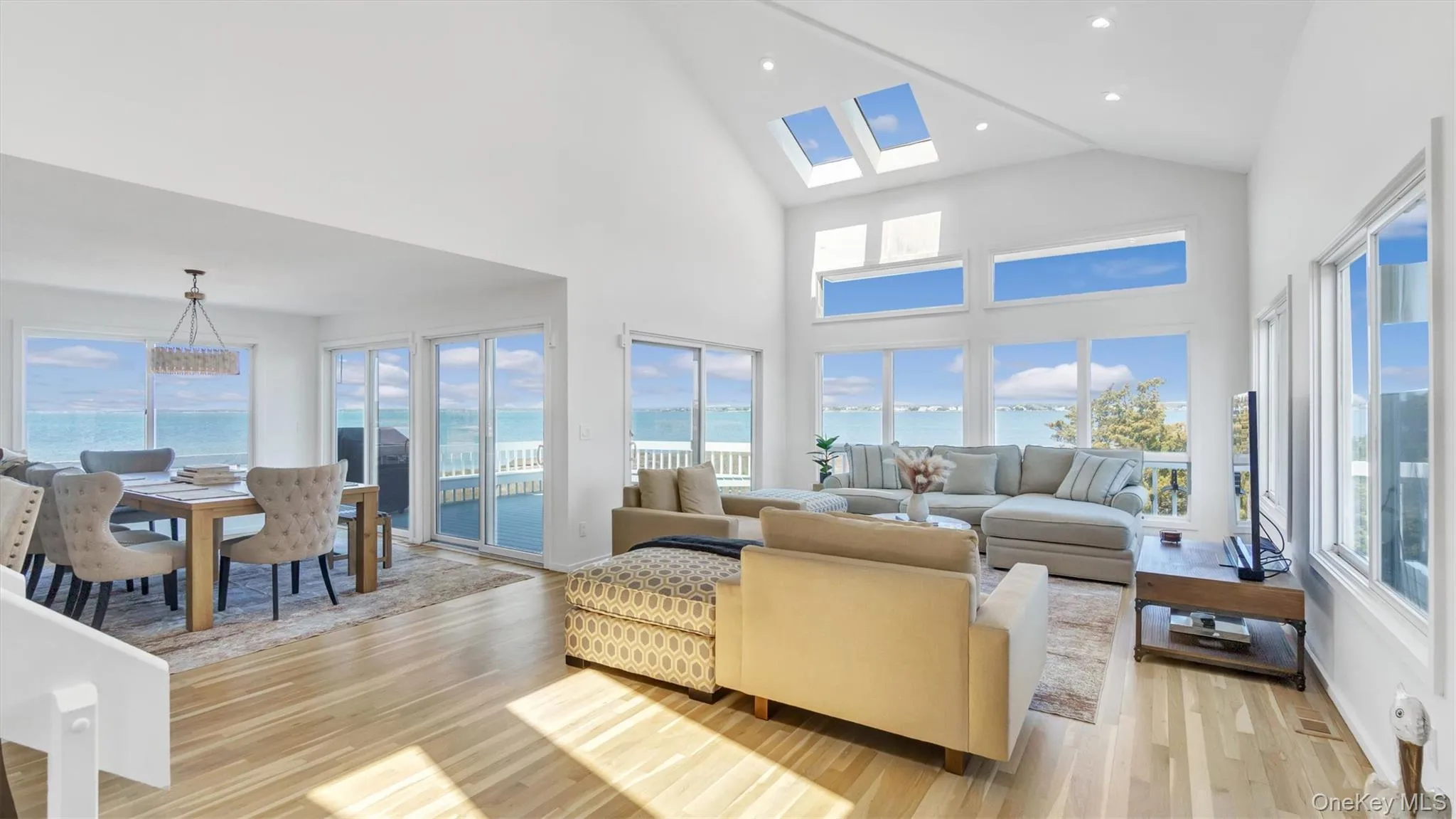 Living room with high vaulted ceiling, a skylight, light wood finished floors, and recessed lighting Living room with high vaulted ceiling, a skylight, light wood finished floors, and recessed lighting