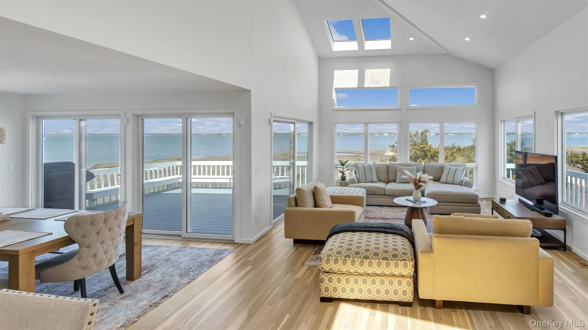 Living area with high vaulted ceiling, a skylight, light wood-style floors, and recessed lighting Living area with high vaulted ceiling, a skylight, light wood-style floors, and recessed lighting