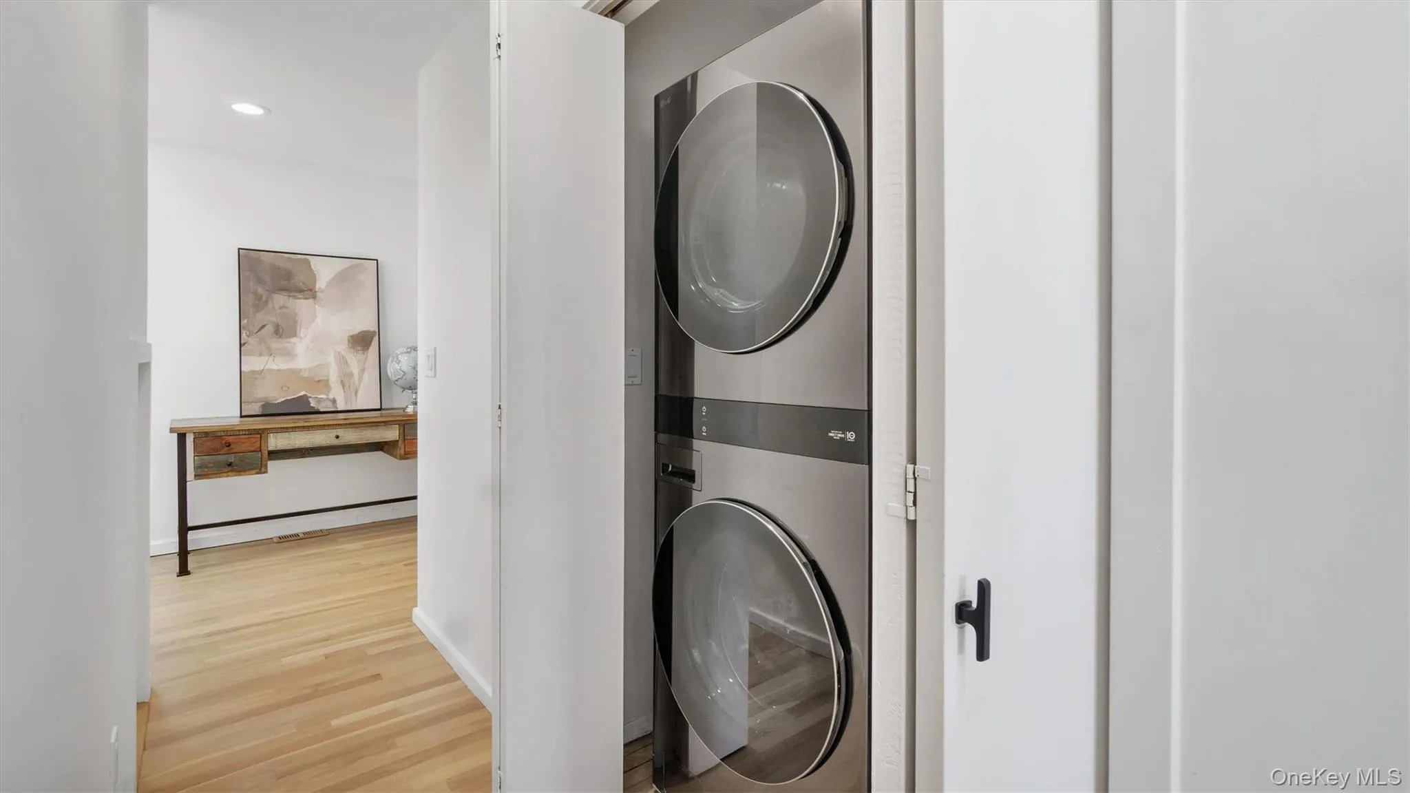 Washroom with stacked washer / drying machine, wood finished floors, and laundry area Washroom with stacked washer / drying machine, wood finished floors, and laundry area