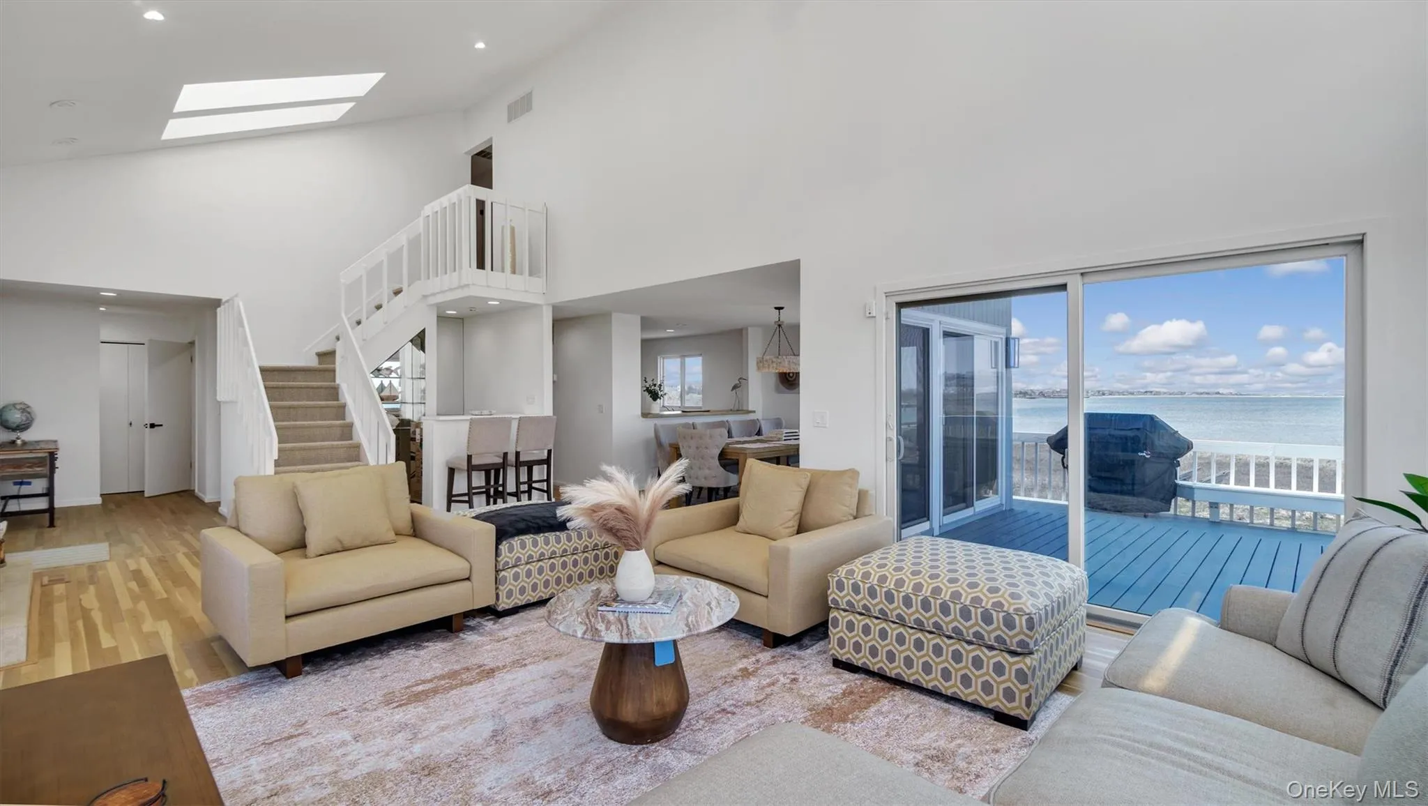 Living area with high vaulted ceiling, a skylight, stairs, and a water view Living area with high vaulted ceiling, a skylight, stairs, and a water view