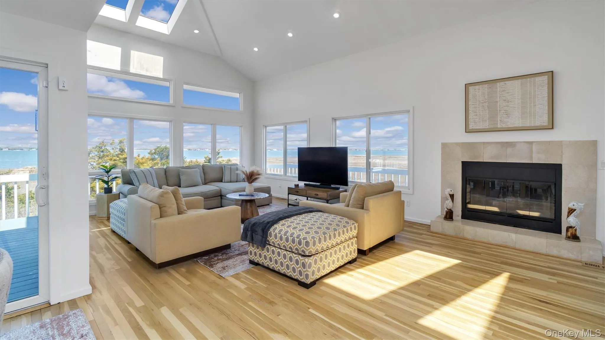 Living area with a tiled fireplace, recessed lighting, a skylight, light wood-style floors, and high vaulted ceiling Living area with a tiled fireplace, recessed lighting, a skylight, light wood-style floors, and high vaulted ceiling