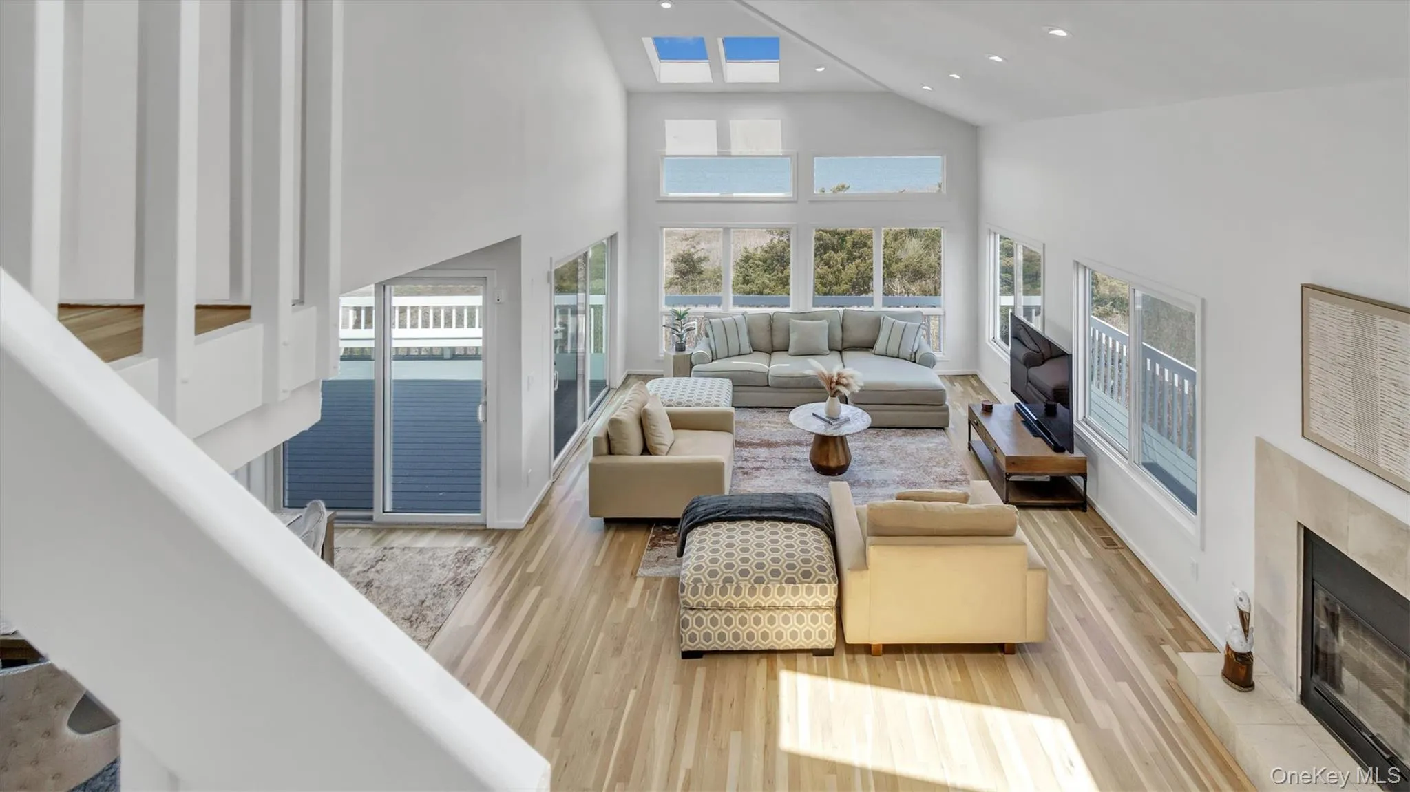 Living area with a tile fireplace, light wood-type flooring, plenty of natural light, and high vaulted ceiling Living area with a tile fireplace, light wood-type flooring, plenty of natural light, and high vaulted ceiling