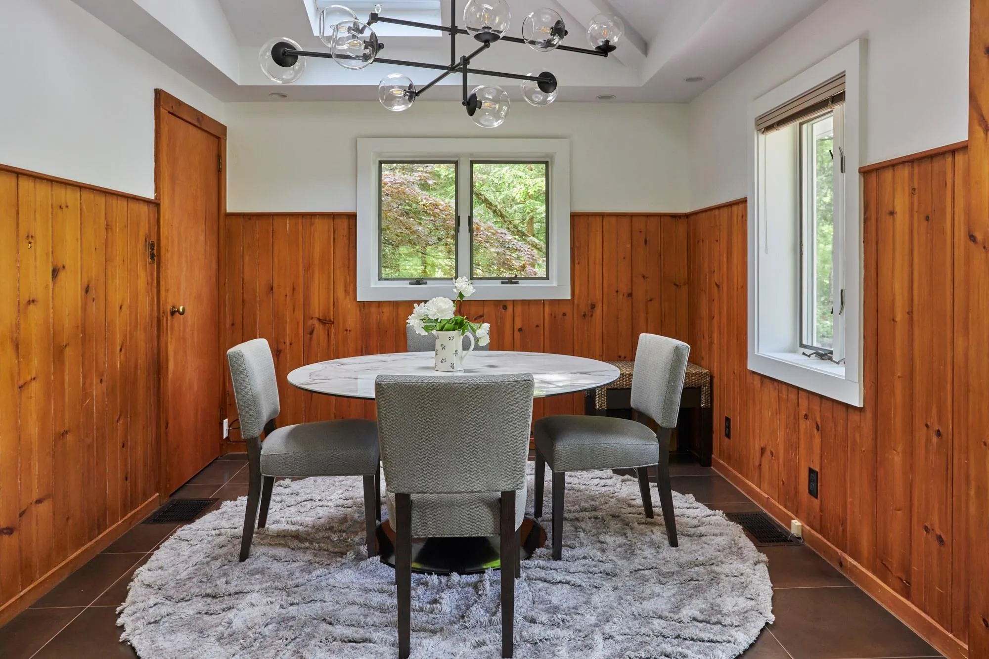 Dining room with a wainscoted wall, dark tile patterned flooring, an inviting chandelier, and wooden walls Dining room with a wainscoted wall, dark tile patterned flooring, an inviting chandelier, and wooden walls