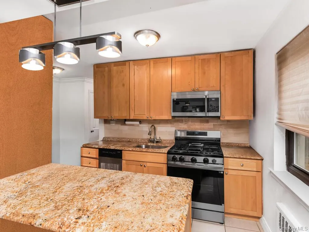Kitchen with light tile patterned flooring, a sink, light stone countertops, stainless steel appliances, and decorative backsplash Kitchen with light tile patterned flooring, a sink, light stone countertops, stainless steel appliances, and decorative backsplash
