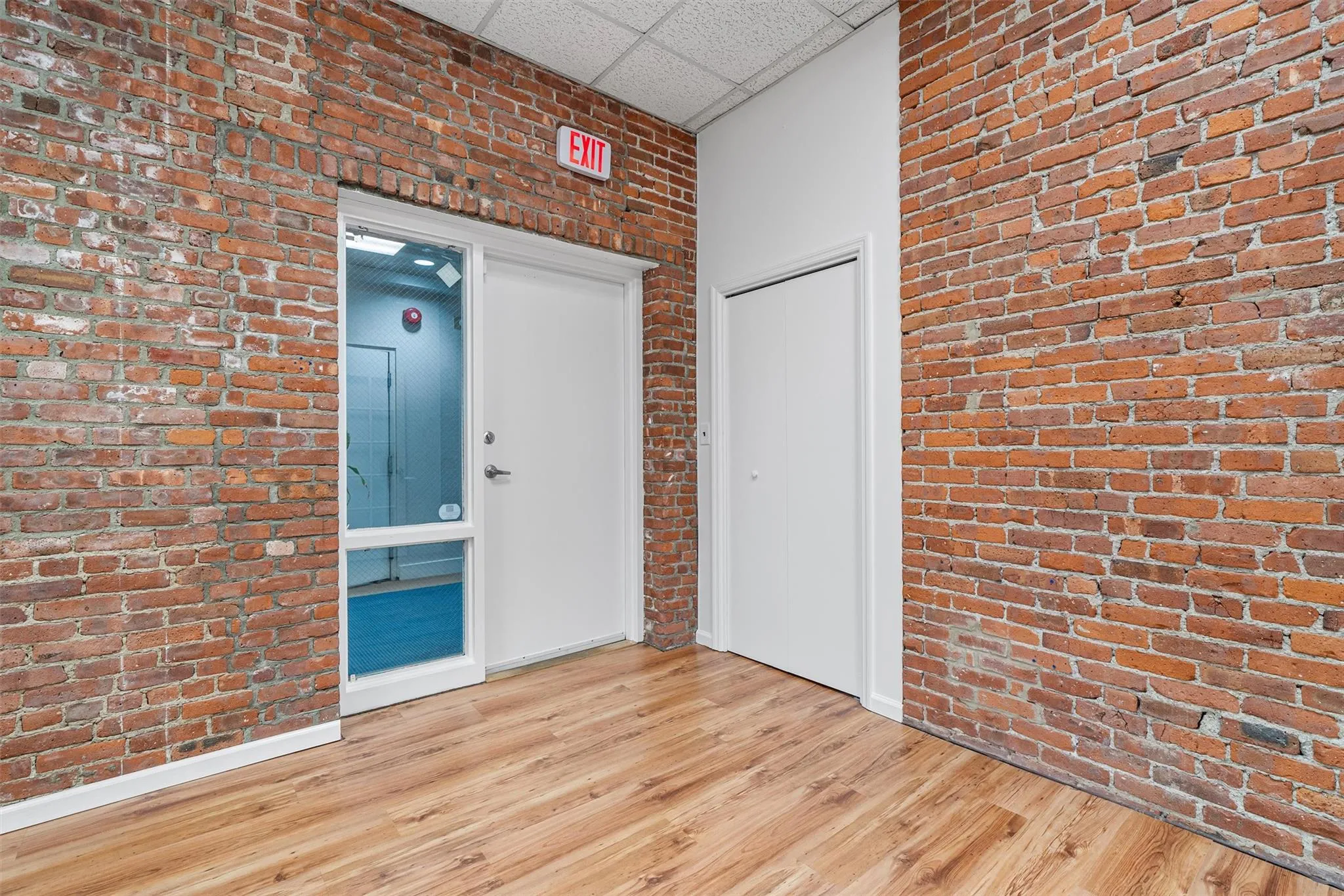 Spare room with wood finished floors, brick wall, and a drop ceiling Spare room with wood finished floors, brick wall, and a drop ceiling