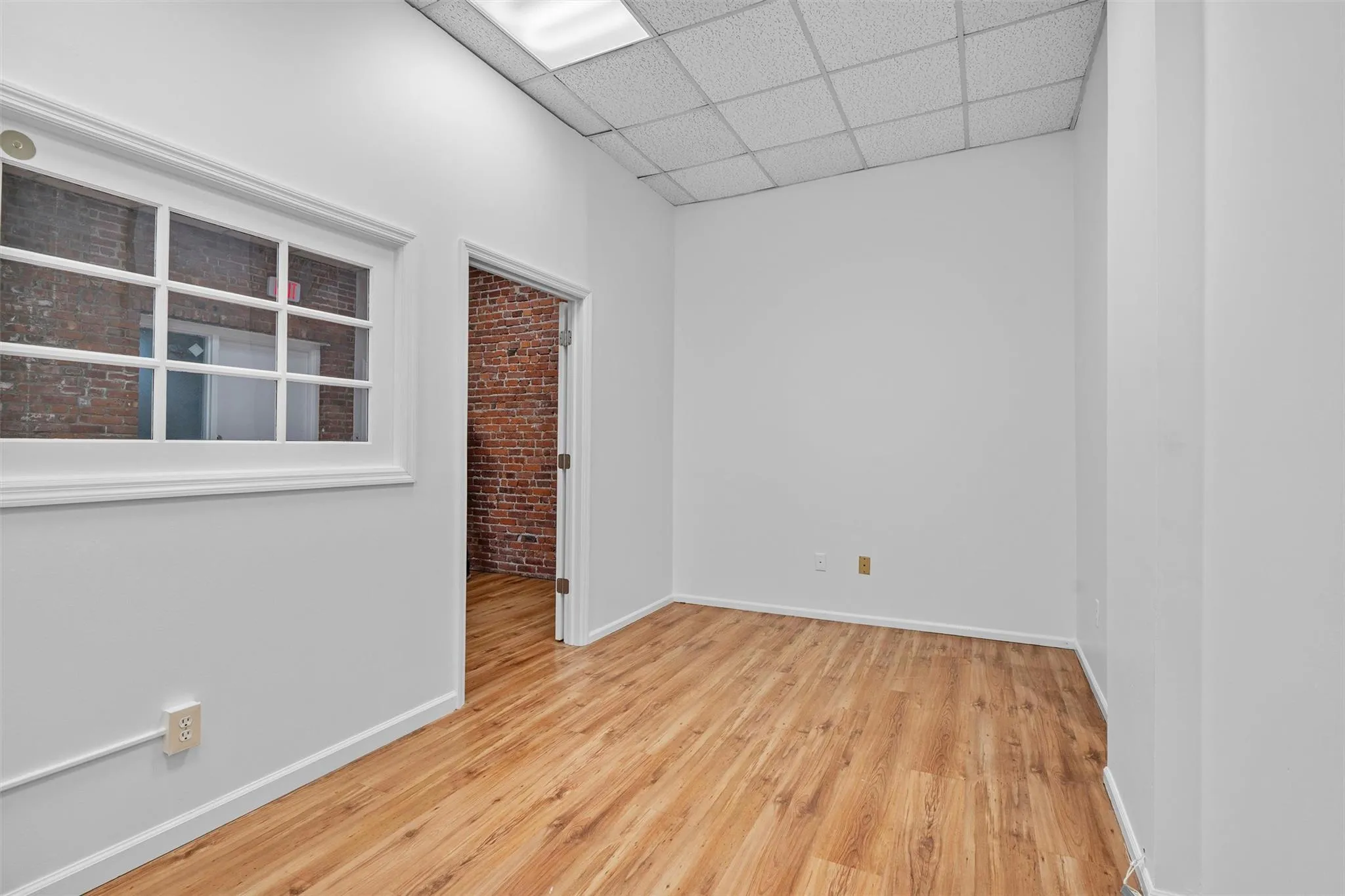 Empty room with a drop ceiling, baseboards, and wood finished floors Empty room with a drop ceiling, baseboards, and wood finished floors