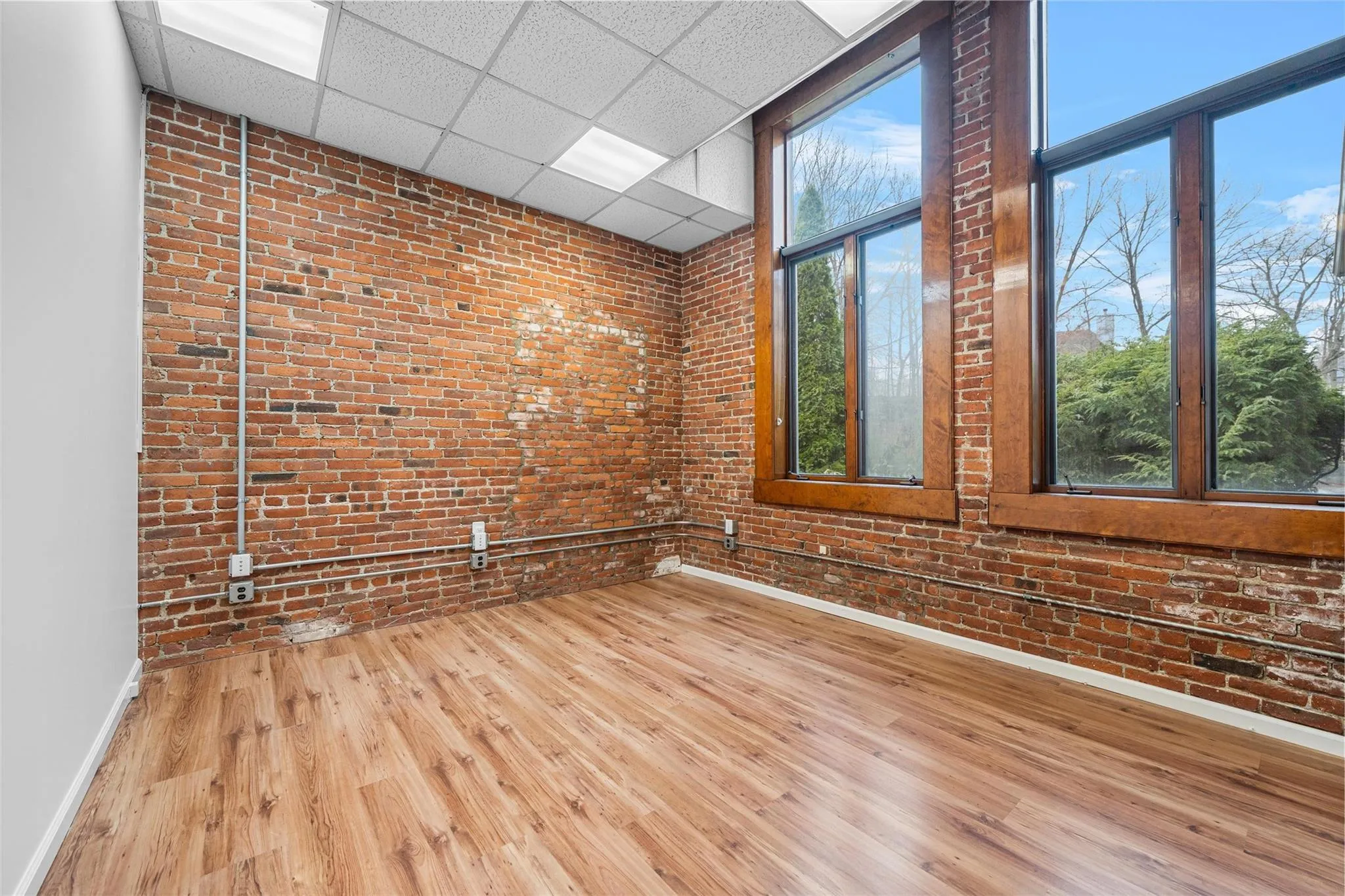 Spare room featuring wood finished floors, brick wall, baseboards, and a paneled ceiling Spare room featuring wood finished floors, brick wall, baseboards, and a paneled ceiling