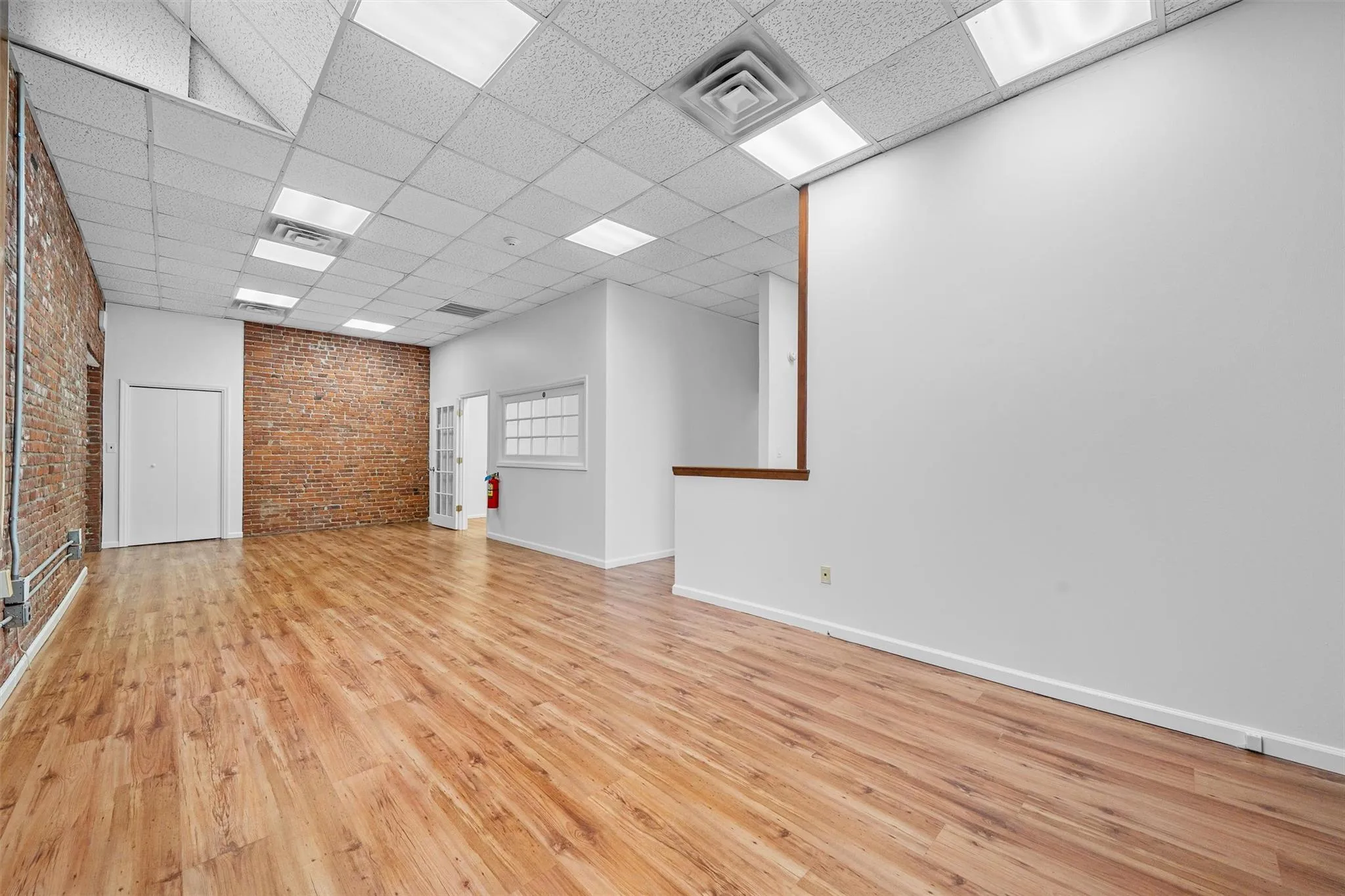 Unfurnished room with visible vents, wood finished floors, brick wall, and a paneled ceiling Unfurnished room with visible vents, wood finished floors, brick wall, and a paneled ceiling