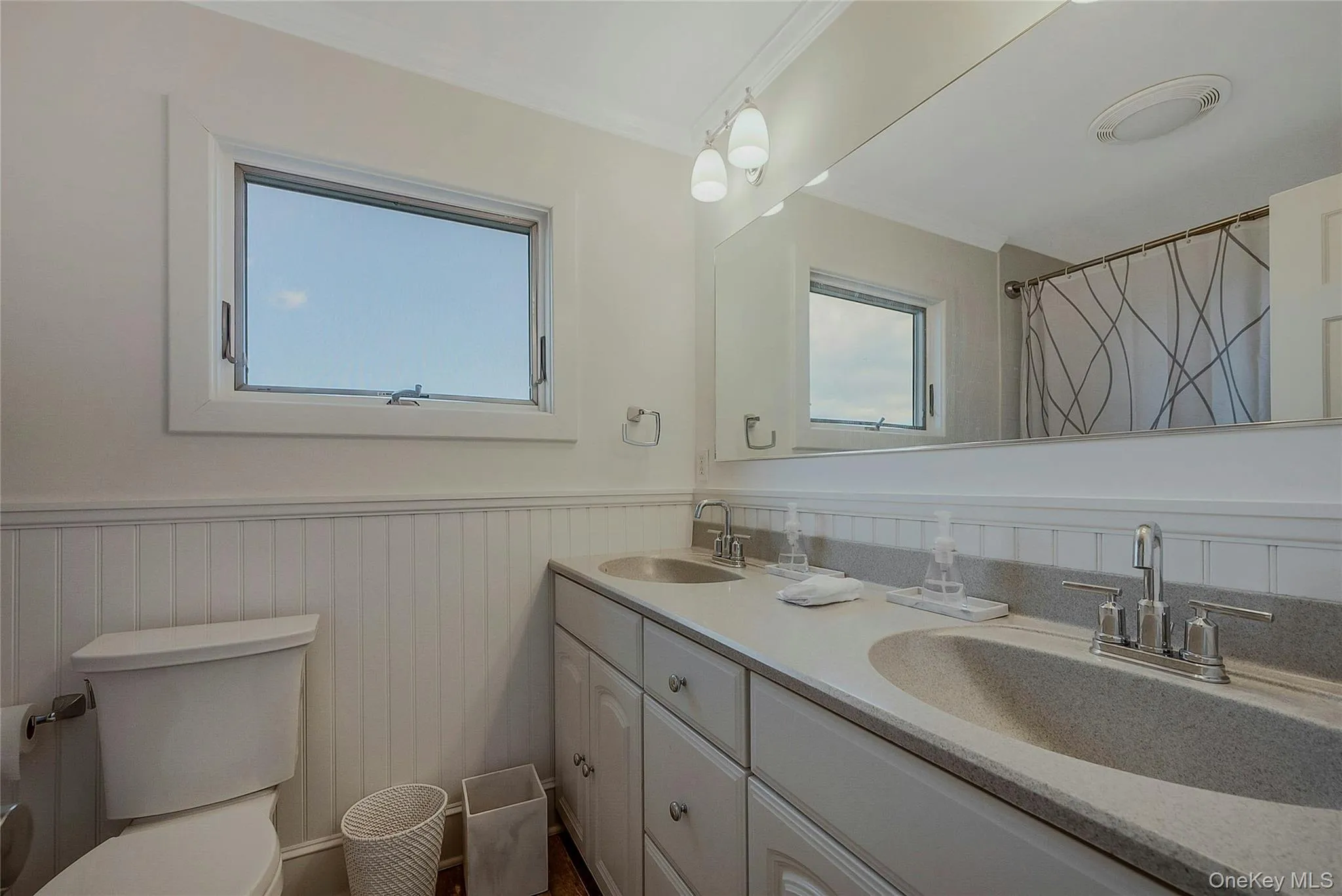 Full bathroom with a wainscoted wall, a sink, toilet, and double vanity Full bathroom with a wainscoted wall, a sink, toilet, and double vanity