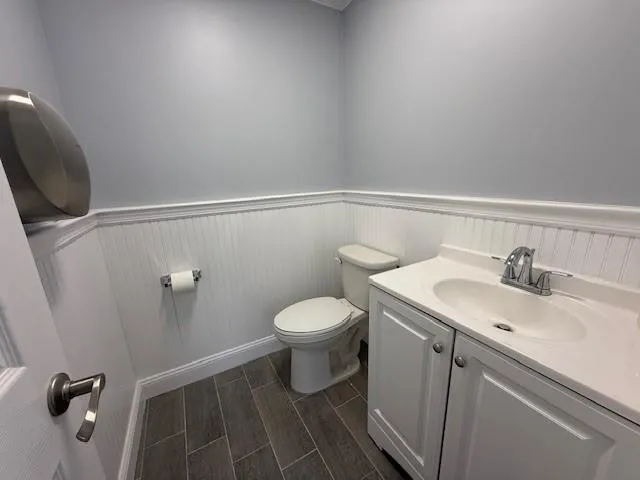 Half bath featuring wainscoting, toilet, vanity, and wood finish floors Half bath featuring wainscoting, toilet, vanity, and wood finish floors