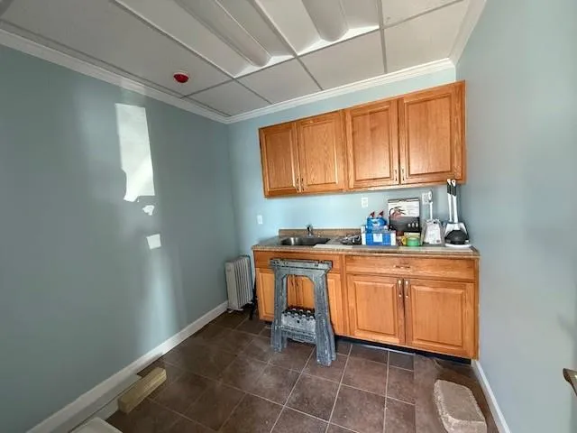 Kitchen featuring crown molding, a sink, radiator, dark tile patterned floors, and baseboards Kitchen featuring crown molding, a sink, radiator, dark tile patterned floors, and baseboards