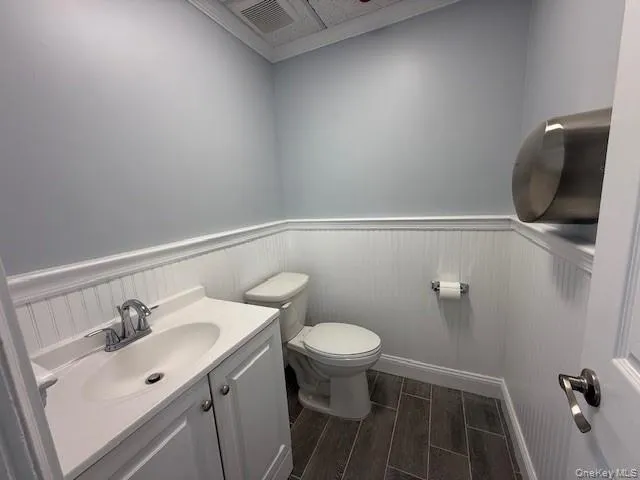 Half bath featuring a wainscoted wall, toilet, wood finish floors, and vanity Half bath featuring a wainscoted wall, toilet, wood finish floors, and vanity