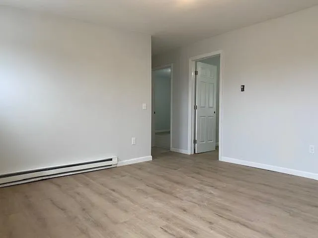 Spare room with a baseboard radiator, wood finished floors, and baseboards Spare room with a baseboard radiator, wood finished floors, and baseboards