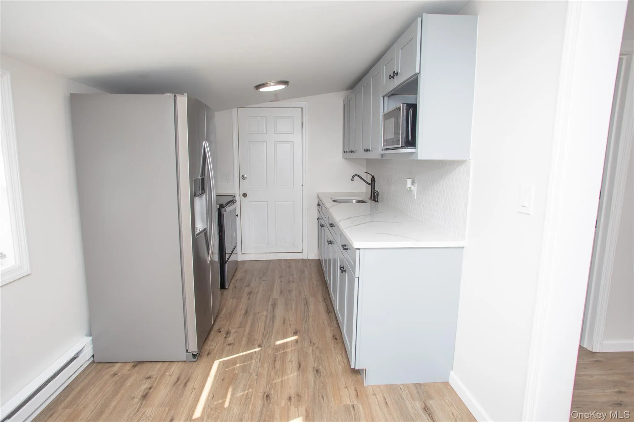 Kitchen with a sink, light stone countertops, appliances with stainless steel finishes, baseboard heating, and light wood-style floors Kitchen with a sink, light stone countertops, appliances with stainless steel finishes, baseboard heating, and light wood-style floors