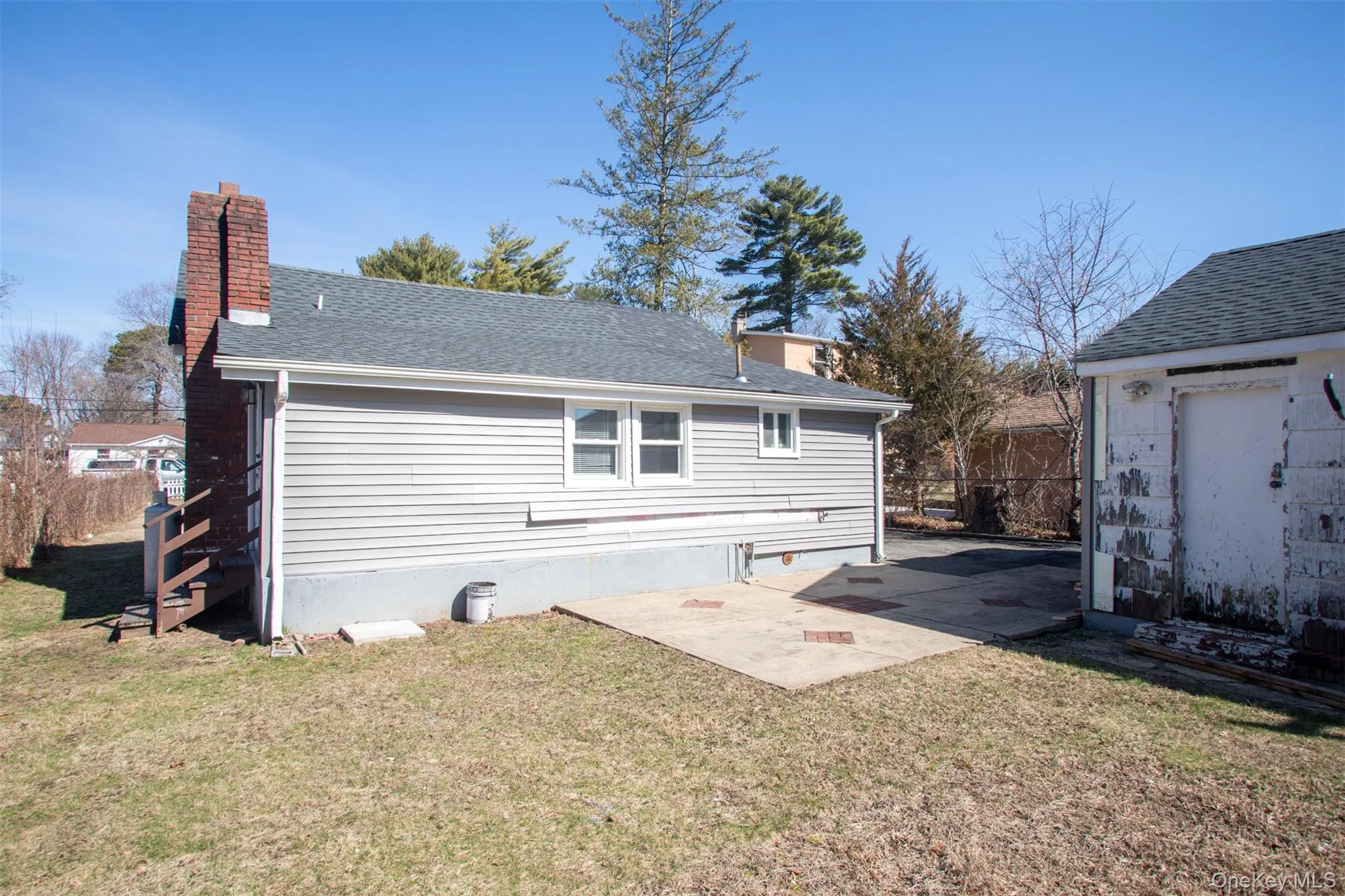 Back of house featuring a patio, a lawn, roof with shingles, and a chimney Back of house featuring a patio, a lawn, roof with shingles, and a chimney