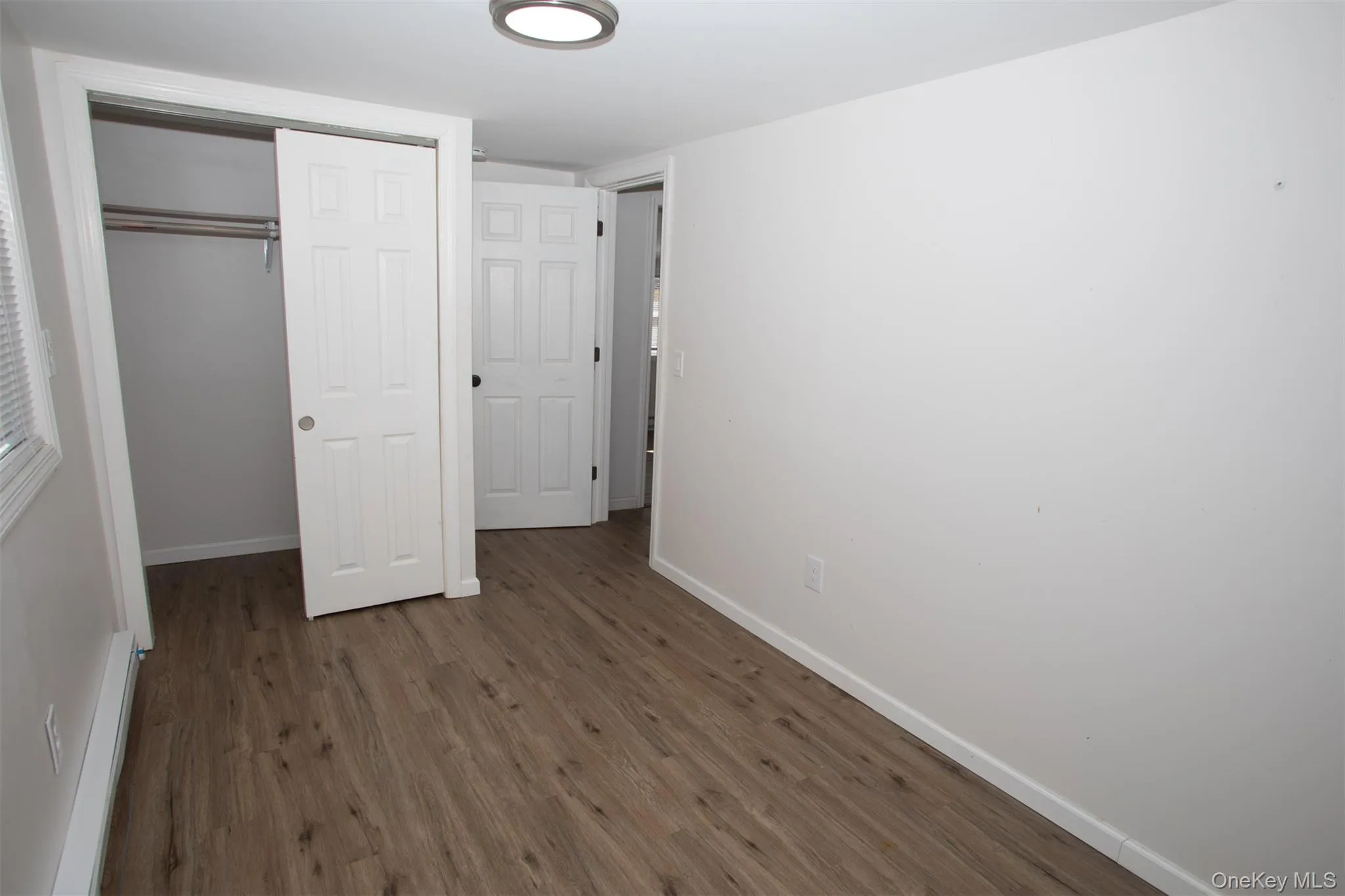 Unfurnished bedroom with baseboards, baseboard heating, a closet, and wood finished floors Unfurnished bedroom with baseboards, baseboard heating, a closet, and wood finished floors