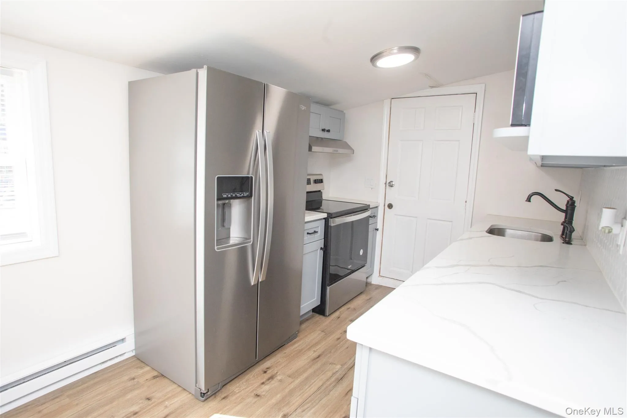 Kitchen featuring a sink, light wood-type flooring, under cabinet range hood, stainless steel appliances, and a baseboard heating unit Kitchen featuring a sink, light wood-type flooring, under cabinet range hood, stainless steel appliances, and a baseboard heating unit