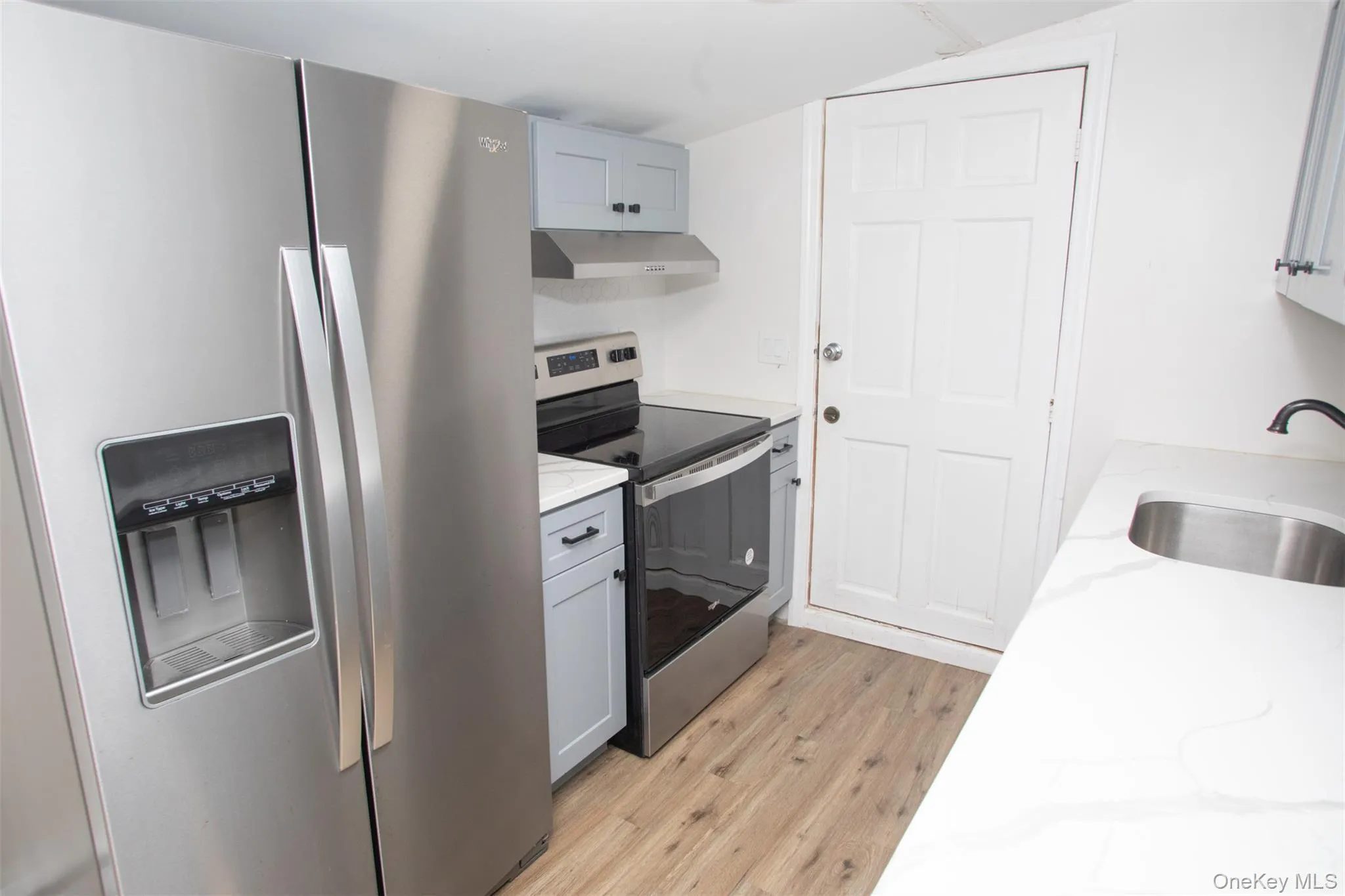 Kitchen with a sink, light wood finished floors, light stone countertops, appliances with stainless steel finishes, and under cabinet range hood Kitchen with a sink, light wood finished floors, light stone countertops, appliances with stainless steel finishes, and under cabinet range hood