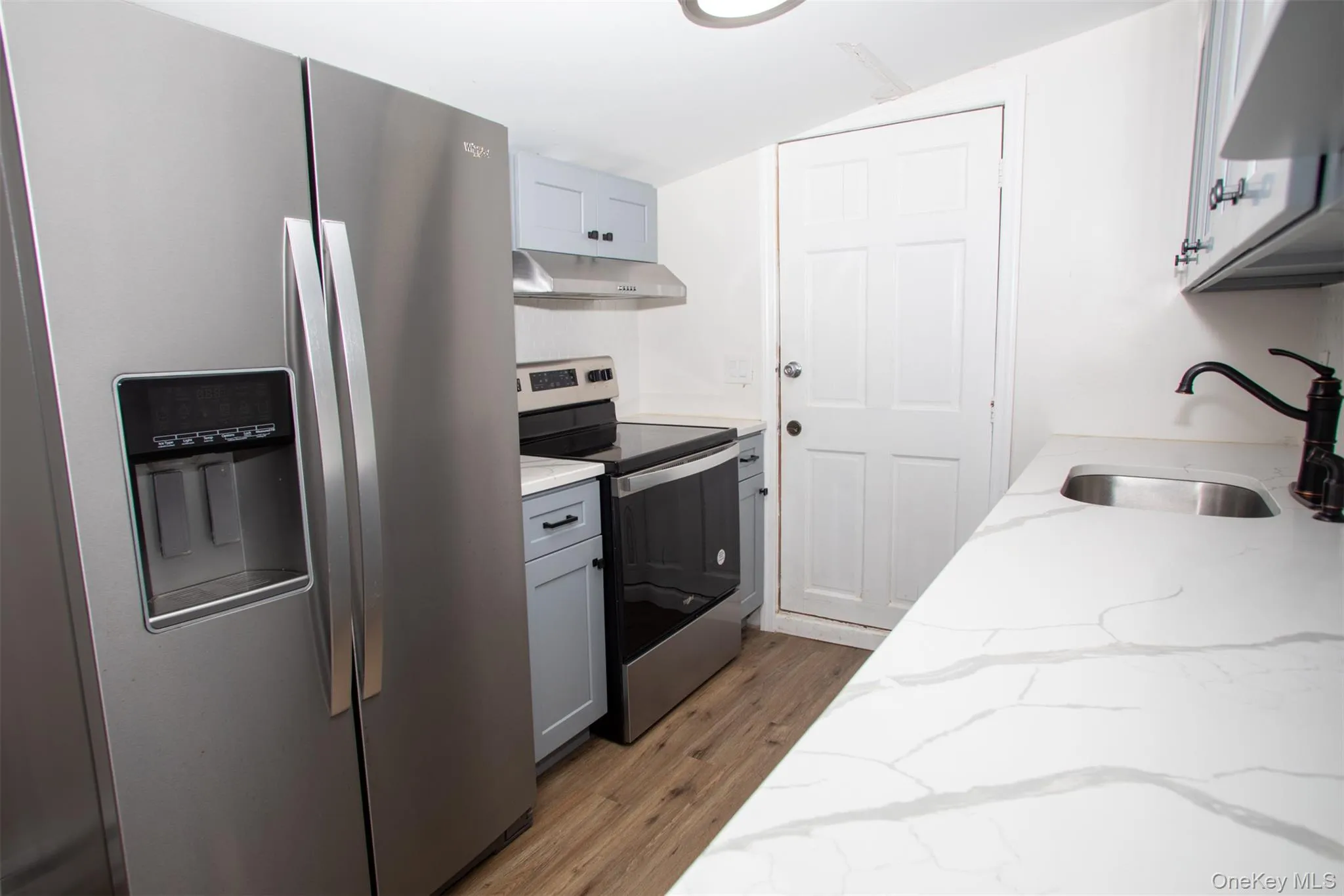 Kitchen with light wood finished floors, light stone countertops, stainless steel appliances, under cabinet range hood, and a sink Kitchen with light wood finished floors, light stone countertops, stainless steel appliances, under cabinet range hood, and a sink