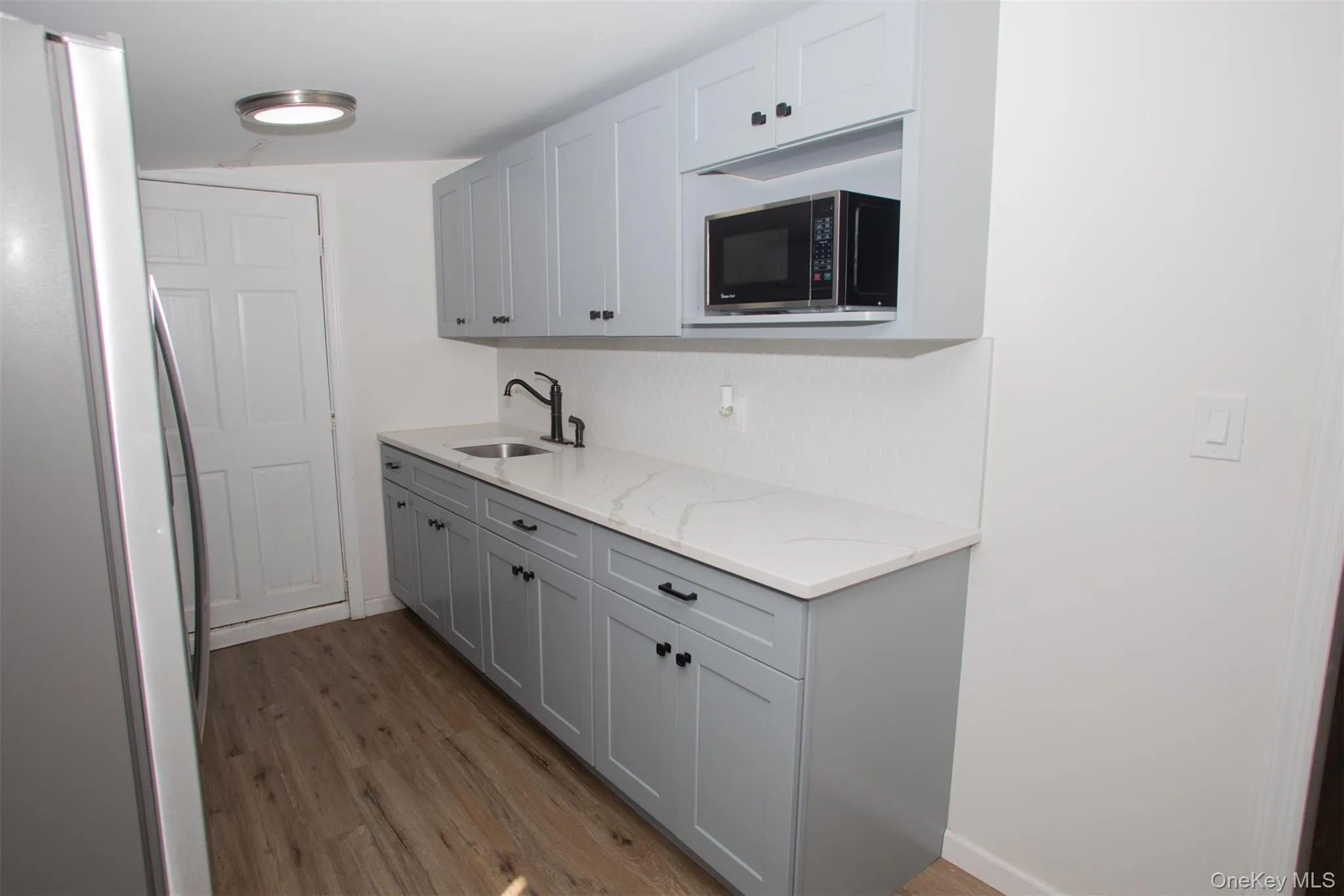 Kitchen with light wood finished floors, baseboards, light stone countertops, a sink, and freestanding refrigerator Kitchen with light wood finished floors, baseboards, light stone countertops, a sink, and freestanding refrigerator