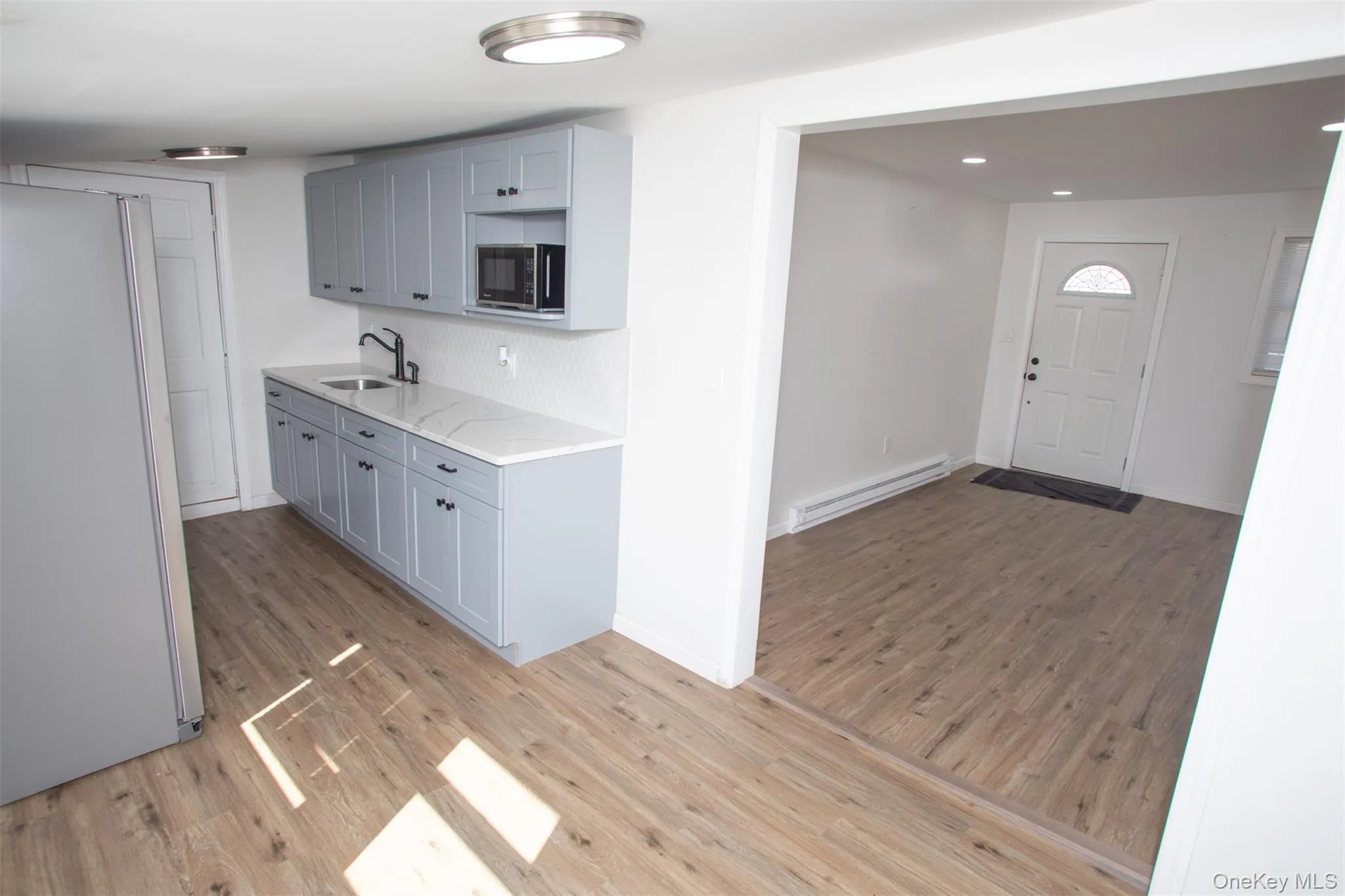 Kitchen featuring decorative backsplash, light wood finished floors, a sink, a baseboard heating unit, and freestanding refrigerator Kitchen featuring decorative backsplash, light wood finished floors, a sink, a baseboard heating unit, and freestanding refrigerator