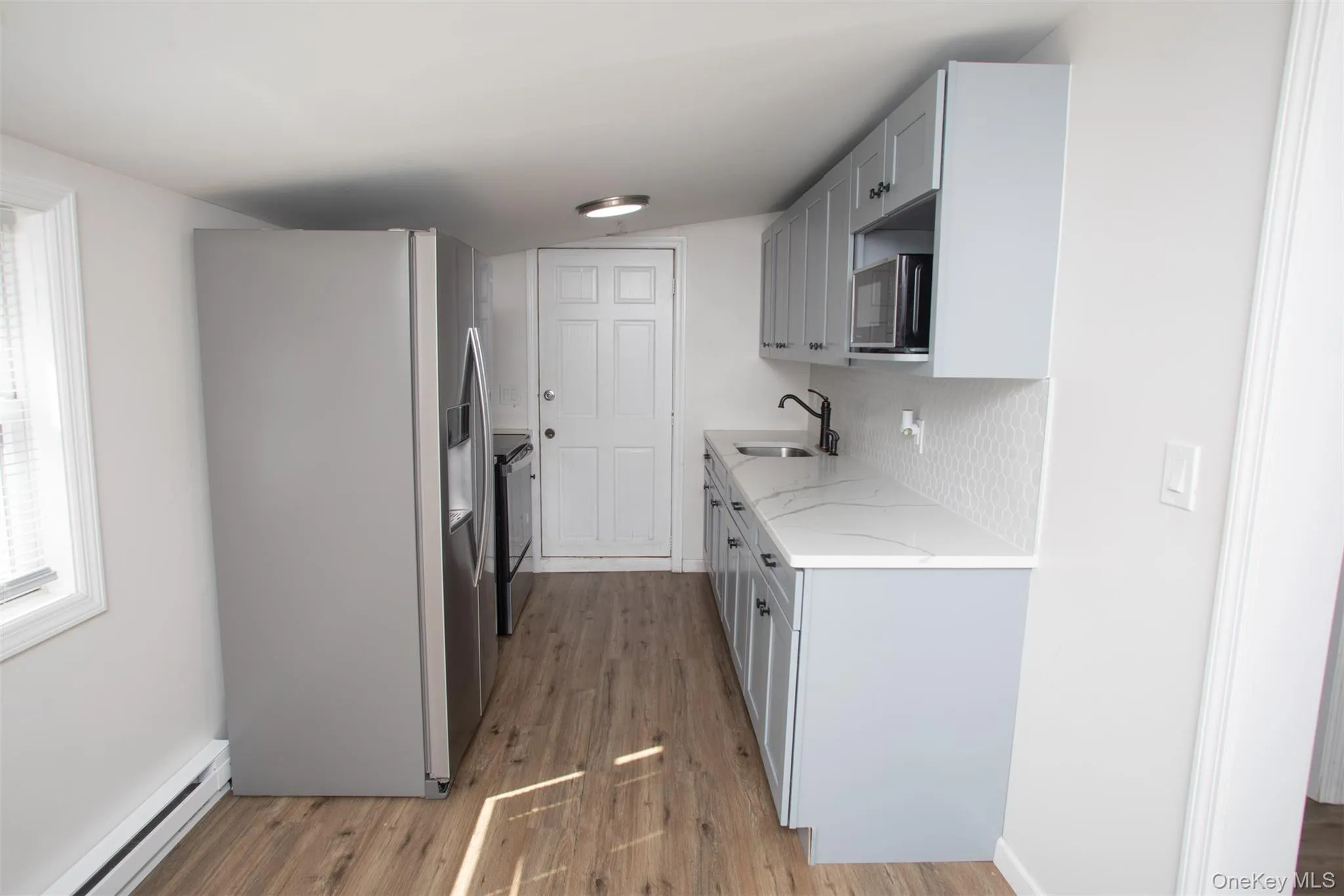 Kitchen featuring a sink, light stone countertops, appliances with stainless steel finishes, baseboard heating, and light wood-style floors Kitchen featuring a sink, light stone countertops, appliances with stainless steel finishes, baseboard heating, and light wood-style floors