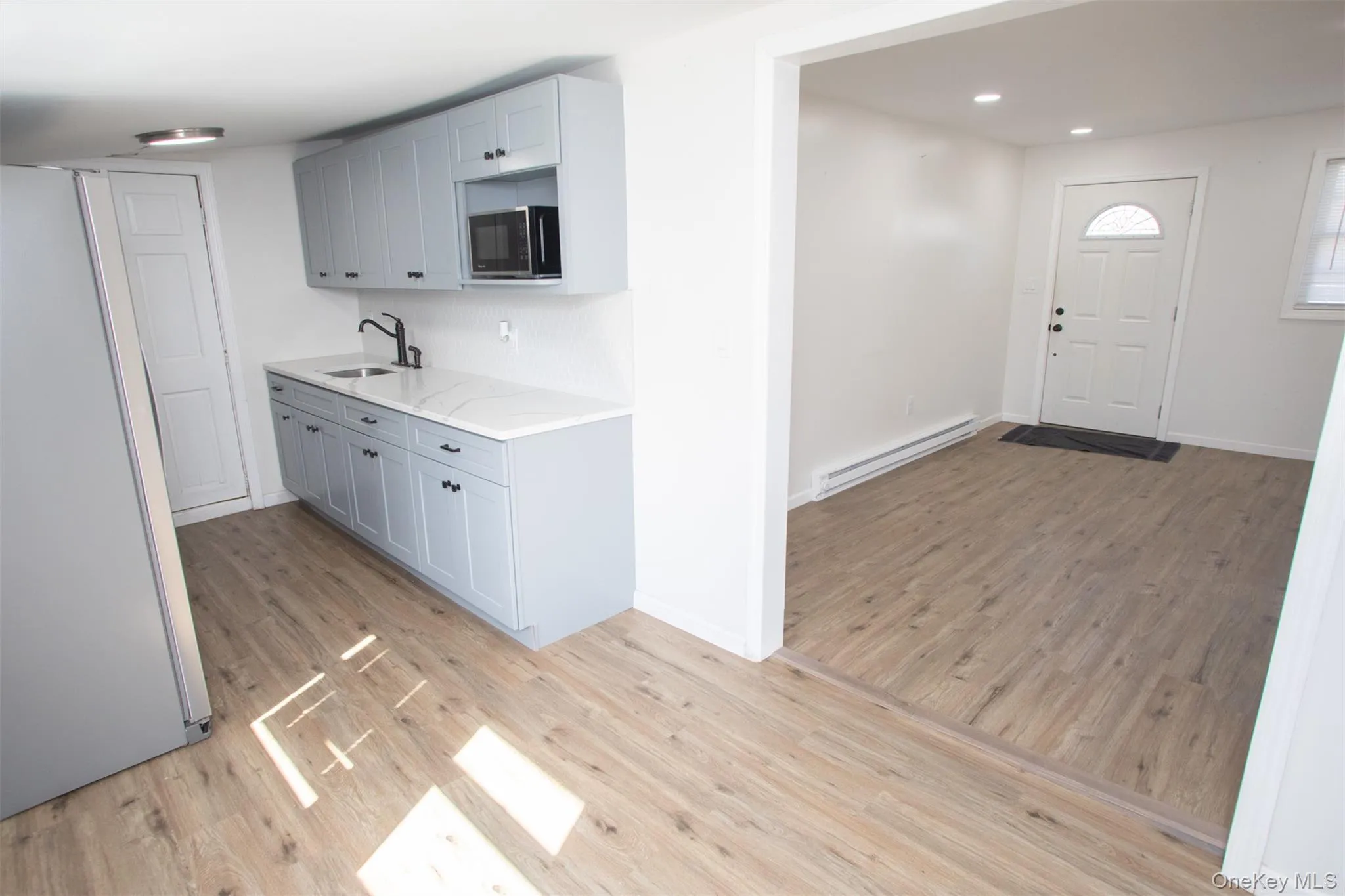 Kitchen featuring baseboards, baseboard heating, a sink, light wood-type flooring, and freestanding refrigerator Kitchen featuring baseboards, baseboard heating, a sink, light wood-type flooring, and freestanding refrigerator