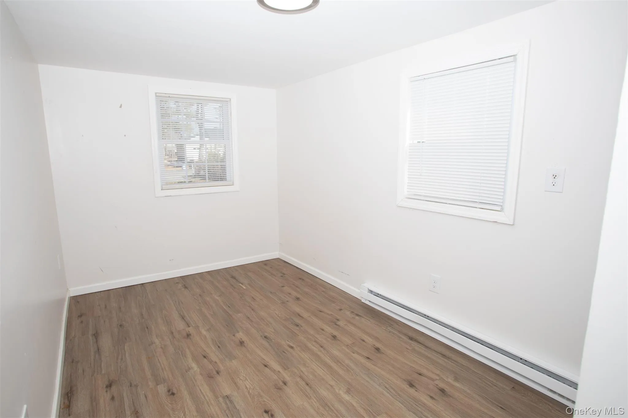 Empty room featuring a baseboard radiator, wood finished floors, and baseboards Empty room featuring a baseboard radiator, wood finished floors, and baseboards