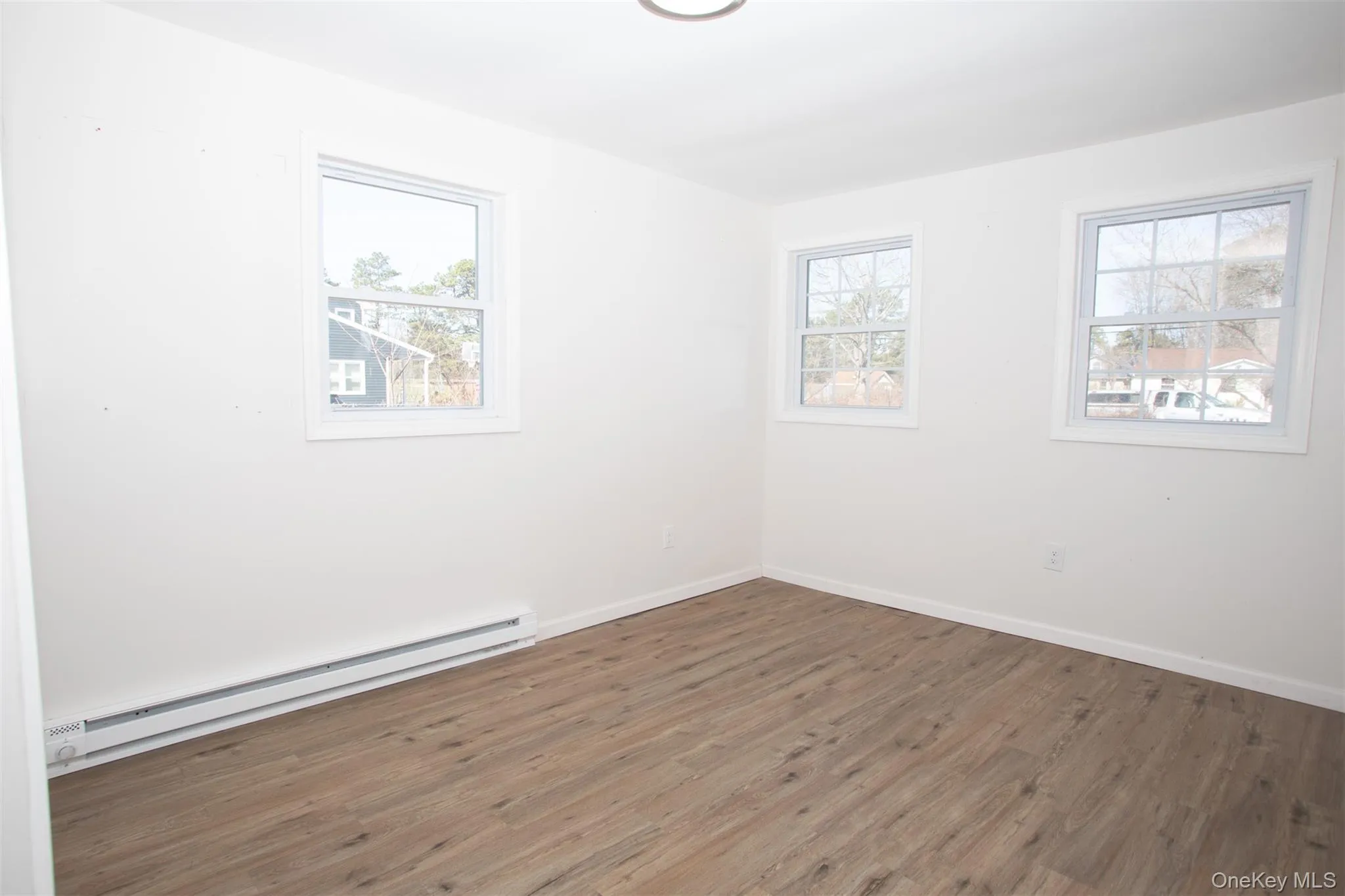 Unfurnished room with baseboards, wood finished floors, and a baseboard heating unit Unfurnished room with baseboards, wood finished floors, and a baseboard heating unit