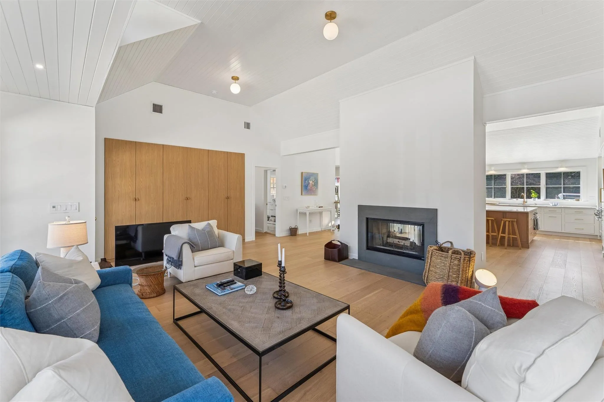 Living area with visible vents, light wood-style floors, lofted ceiling, and a multi sided fireplace Living area with visible vents, light wood-style floors, lofted ceiling, and a multi sided fireplace