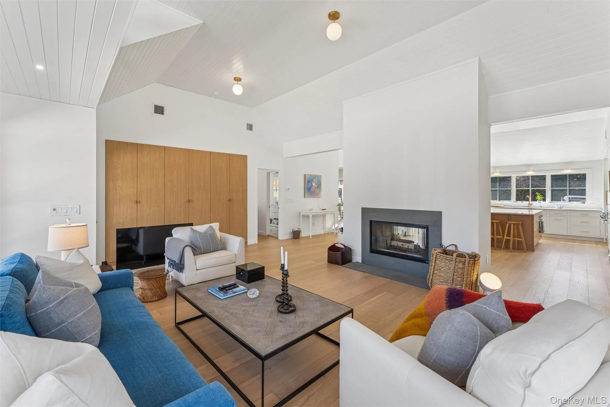 Living area with visible vents, light wood-style floors, lofted ceiling, and a multi sided fireplace Living area with visible vents, light wood-style floors, lofted ceiling, and a multi sided fireplace